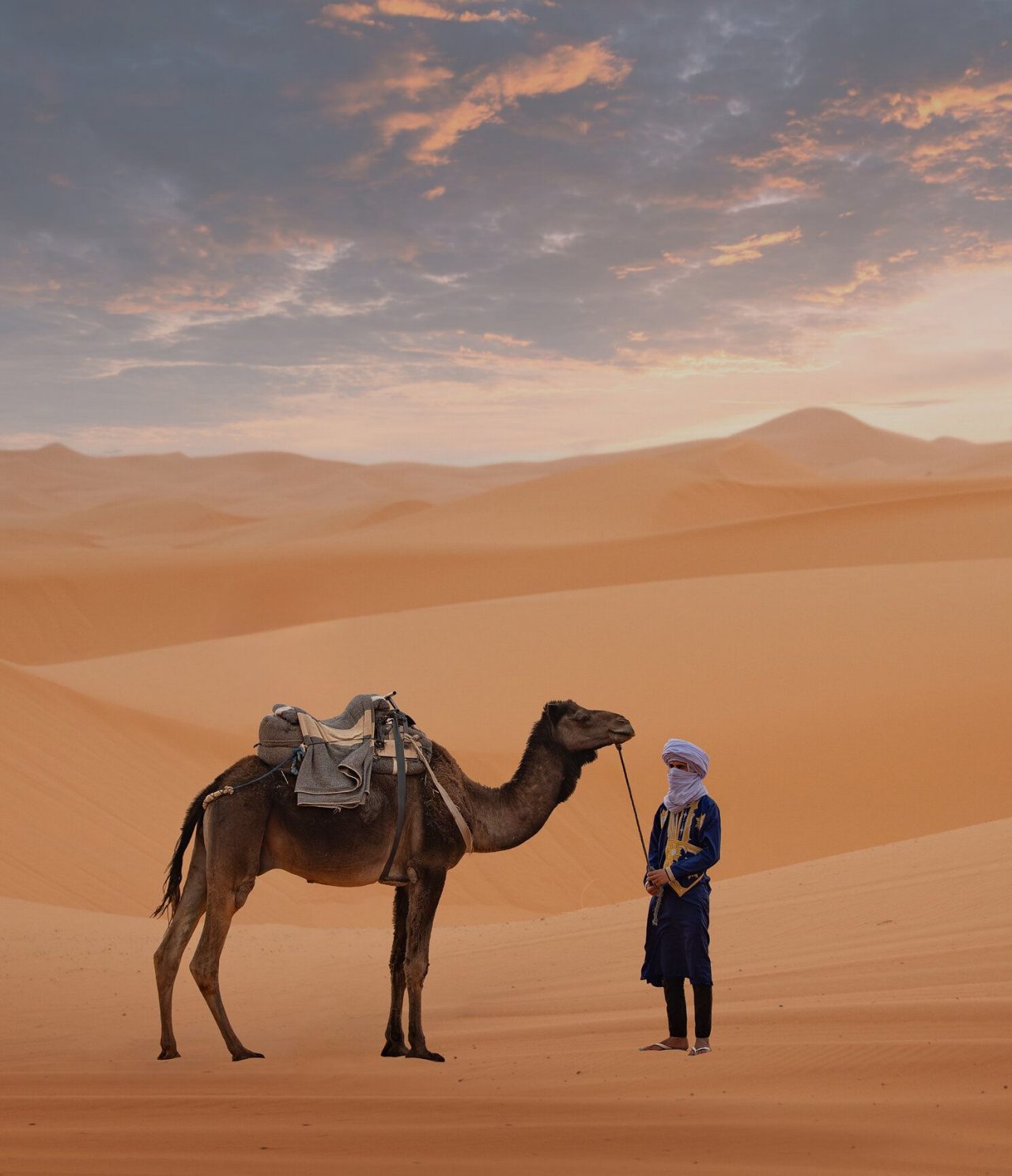 Camello y hombre que lo acompaña, en medio de un gran desierto cerca de Marrakech, con varias dunas en el horizonte