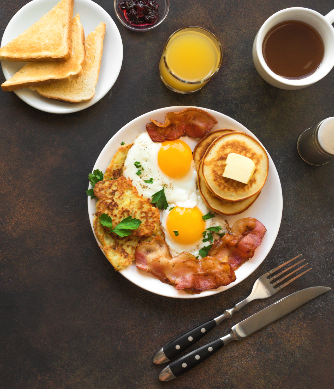 Comida típica de pequeno almoço americano com ovos, bacon, panquecas e torradas, e um sumo de laranja e café para acompanhar