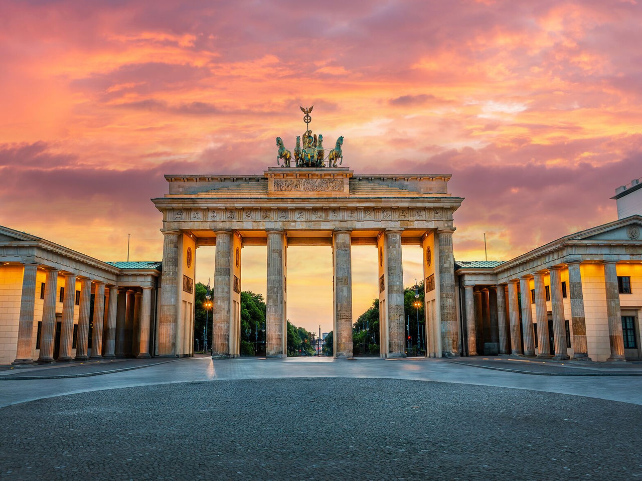 Explora Hoteles en Berlín con vistas a la Puerta de Brandeburgo iluminada bajo un cielo rosado al atardecer