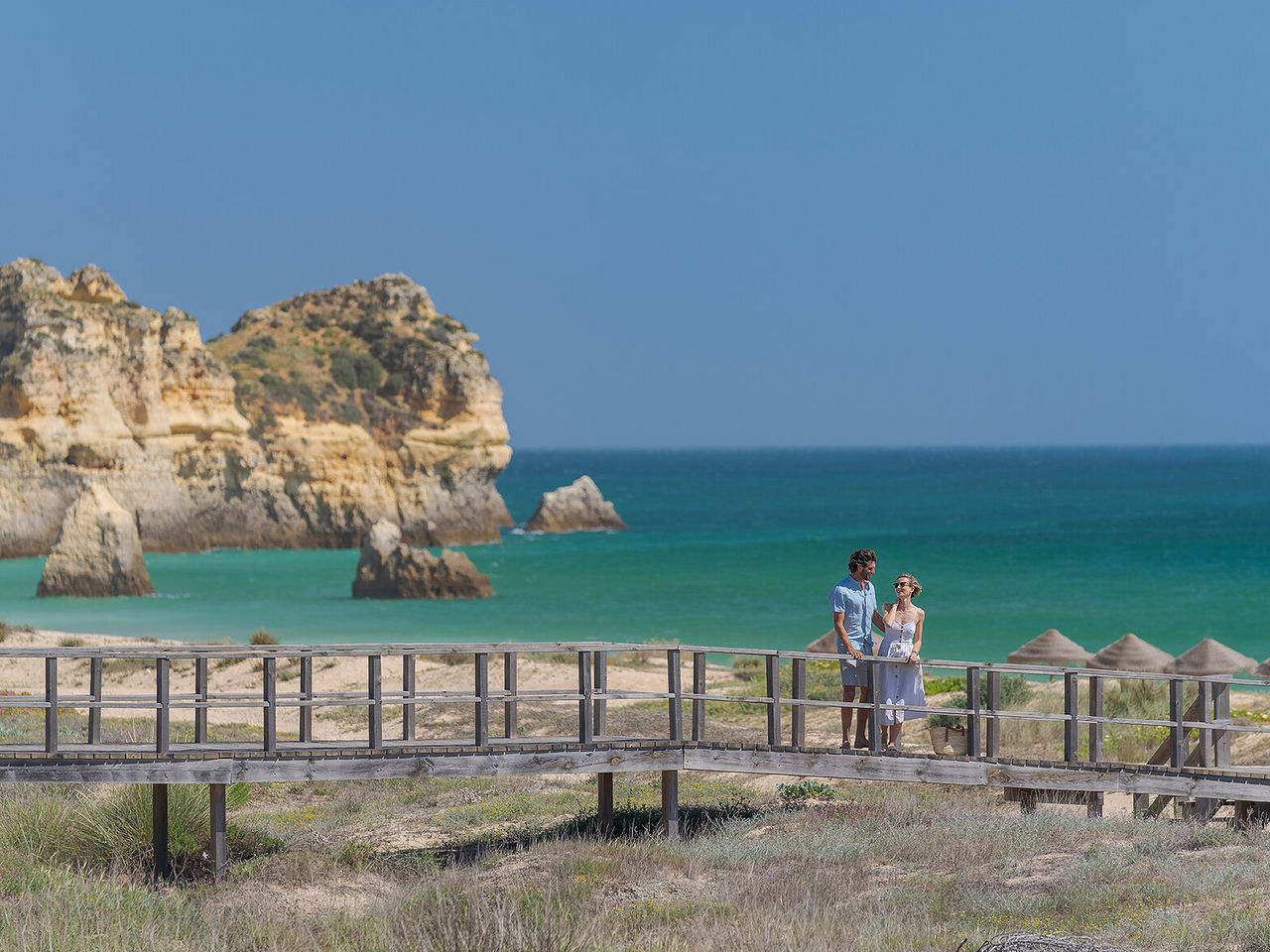 Pareja admirando la vista de una playa en Alvor, Algarve, mientras pasean por los pasadizos junto al mar