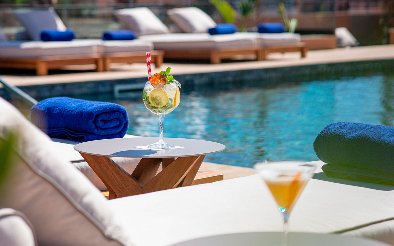 La marca Pestana CR7 Lifestyle Hotels presenta cócteles junto a una piscina con reposeras y toallas azules