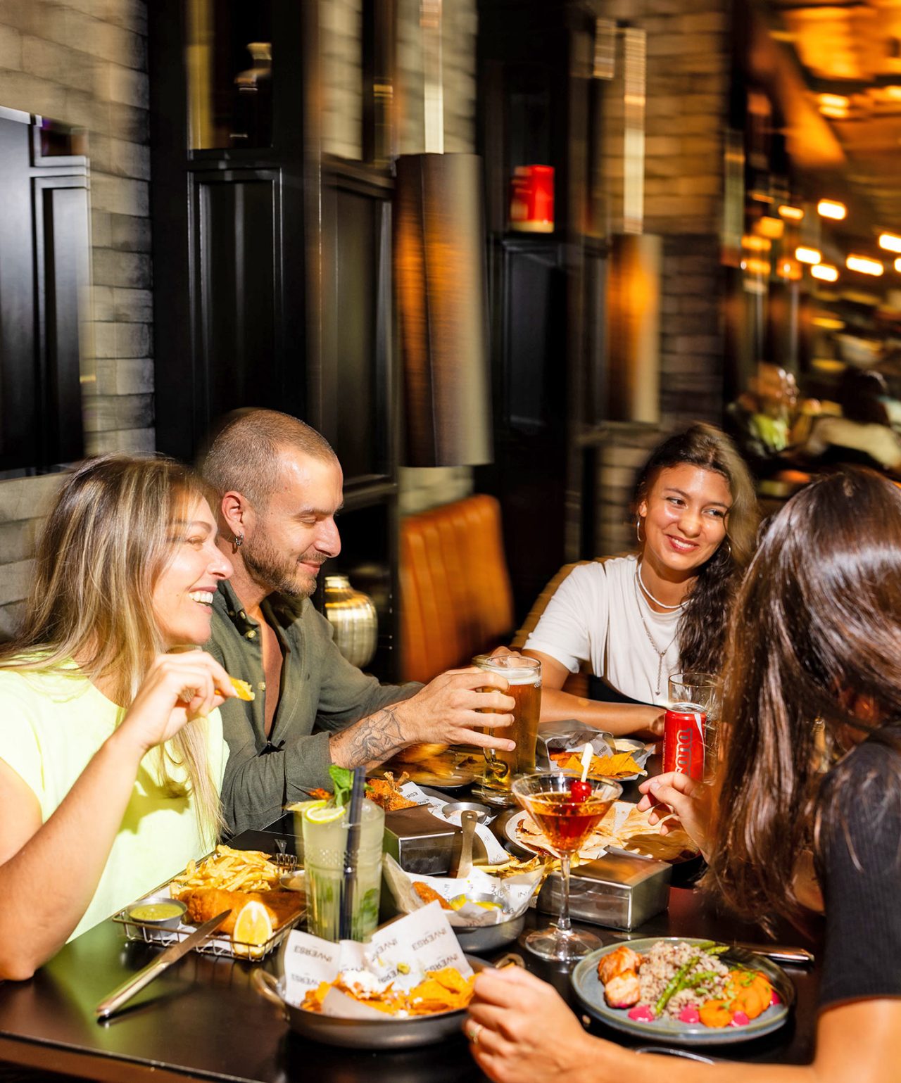 La marca Pestana CR7 Lifestyle Hotels, donde amigos comparten bebidas y platos en un restaurante con luces cálidas