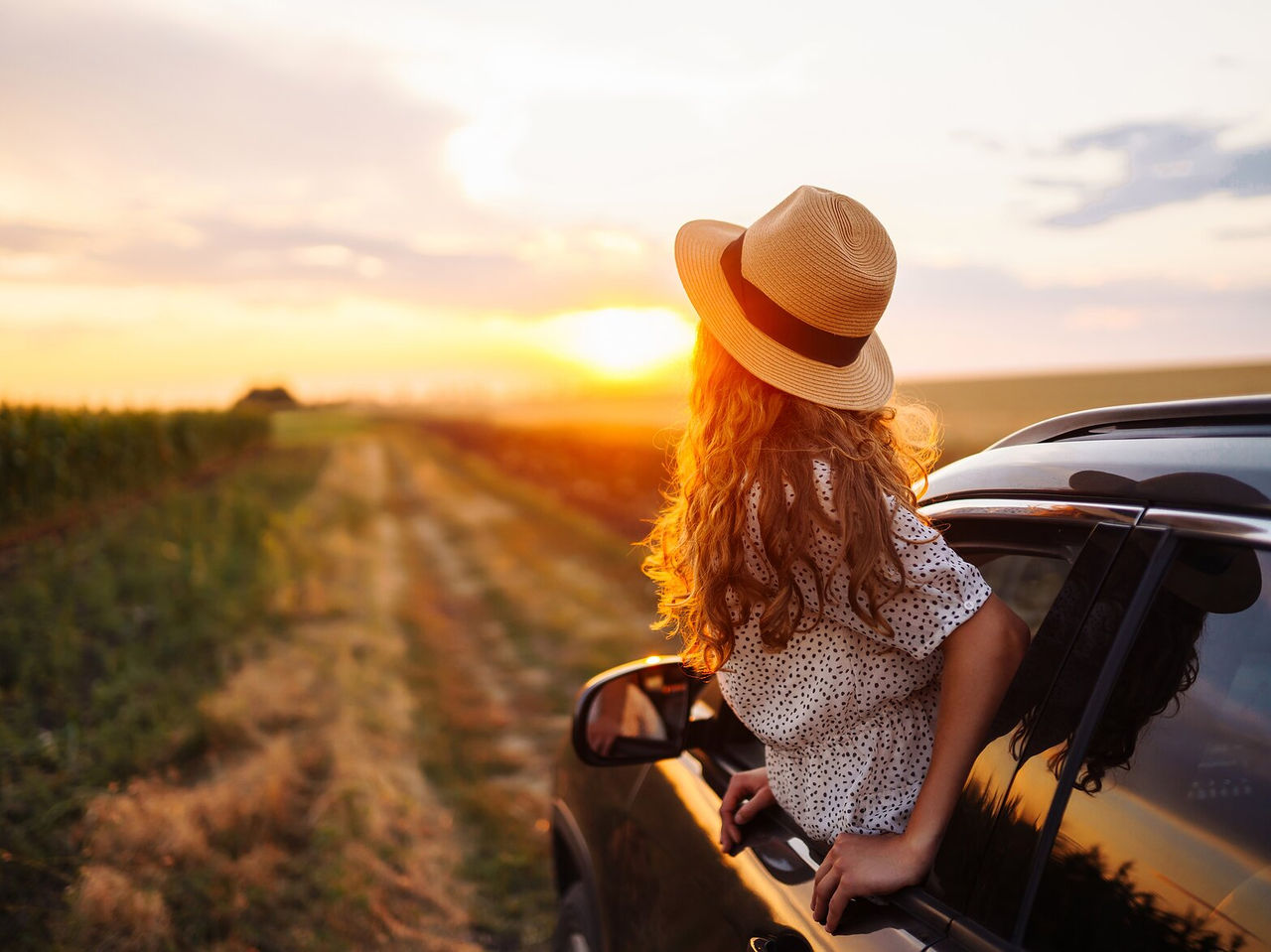 Pessoa a espreitar pela janela de um carro enquanto viaja pelo Alentejo ao pôr do sol, com paisagens deslumbrantes
