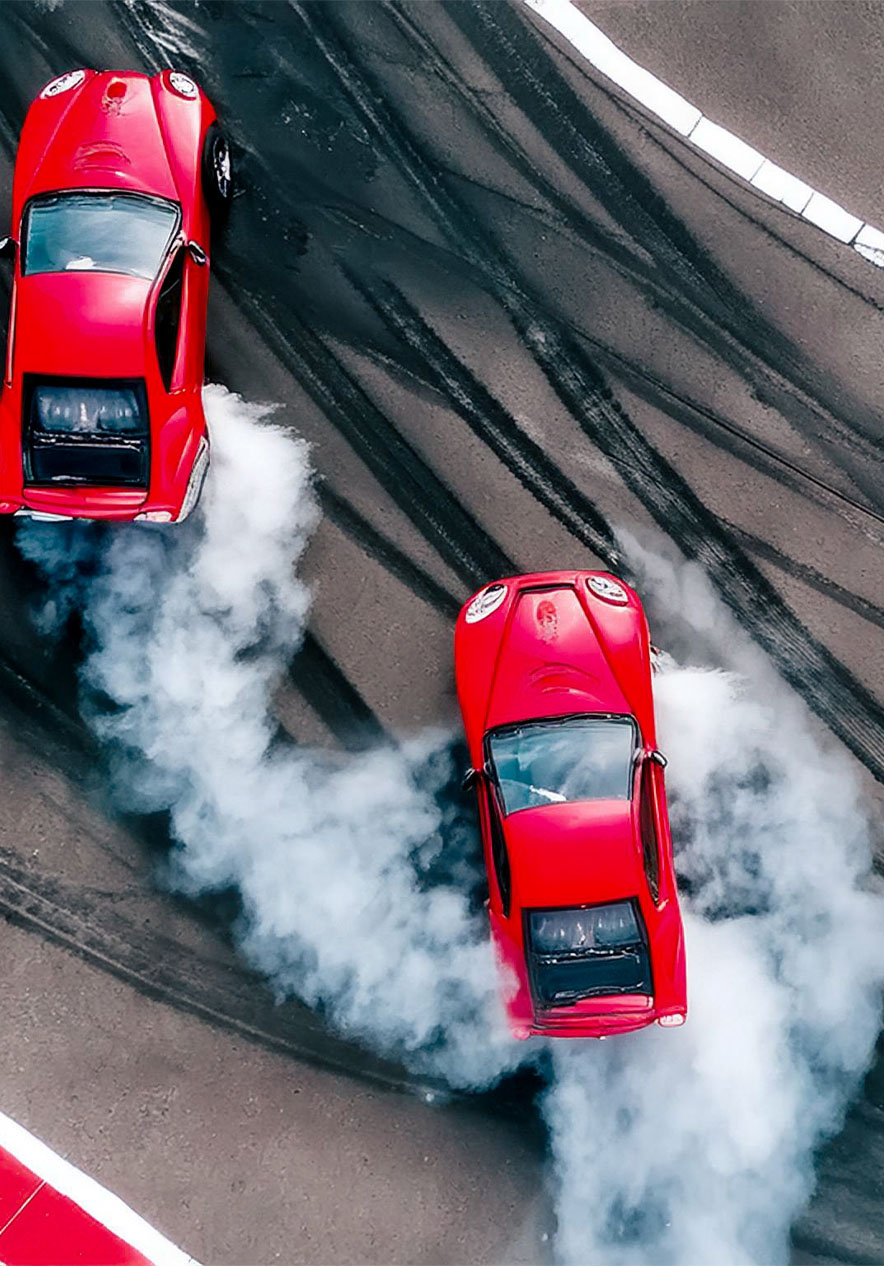 Pista de corrida de carros com automóveis vermelhos a fazerem travagens e a deitar fumo