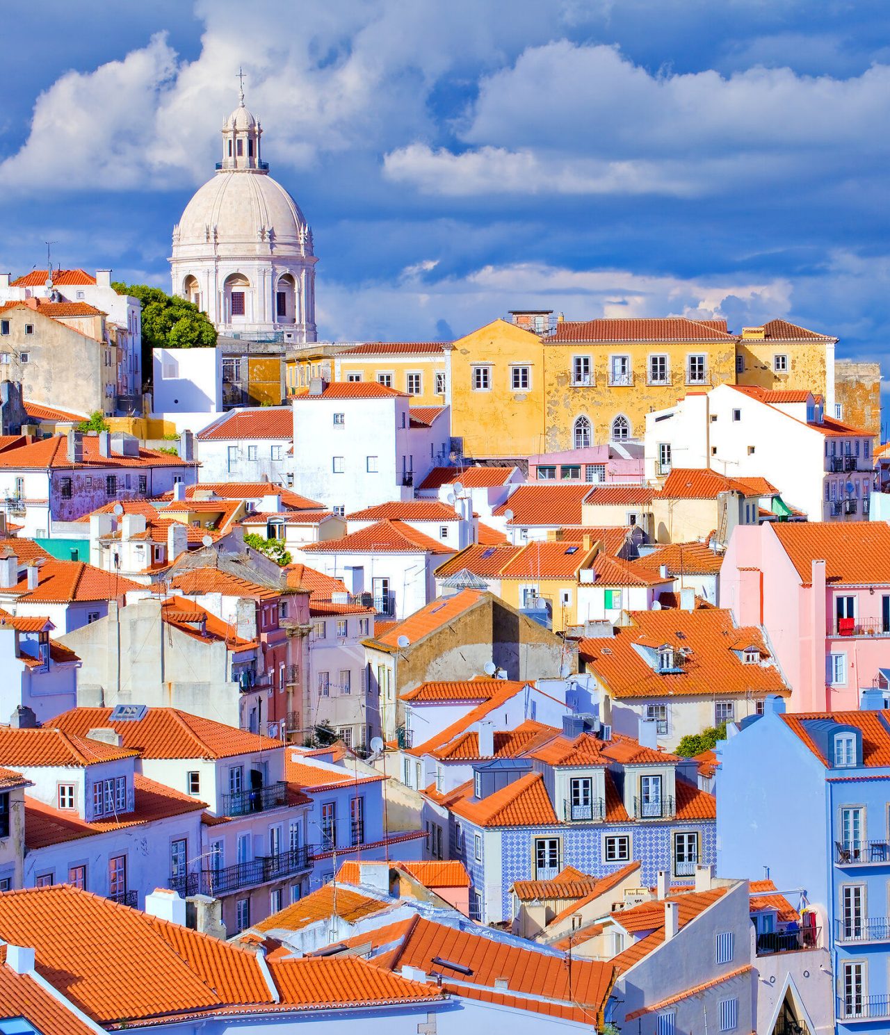 Centro histórico de Lisboa, com vários prédios típicos, com telhados em tijolo e uma basílica ao fundo
