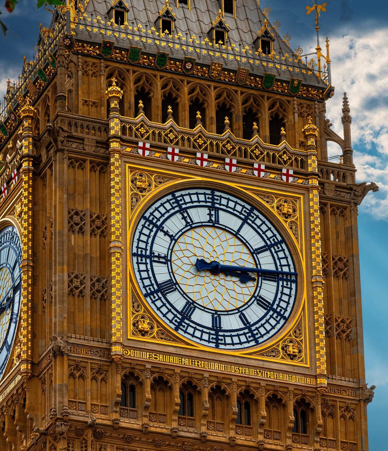 Vista aproximada do famoso relógio Big Ben, com os seus detalhes em dourado, ponteiros pretos e o símbolo de Inglaterra