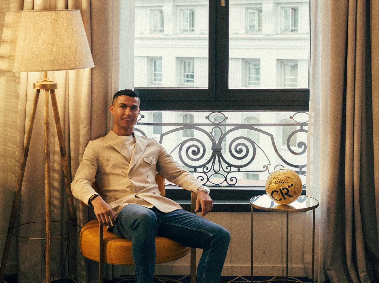 a marca Pestana CR7 Lifestyle Hotels apresentando homem sentado perto da janela com bola dourada na mesa