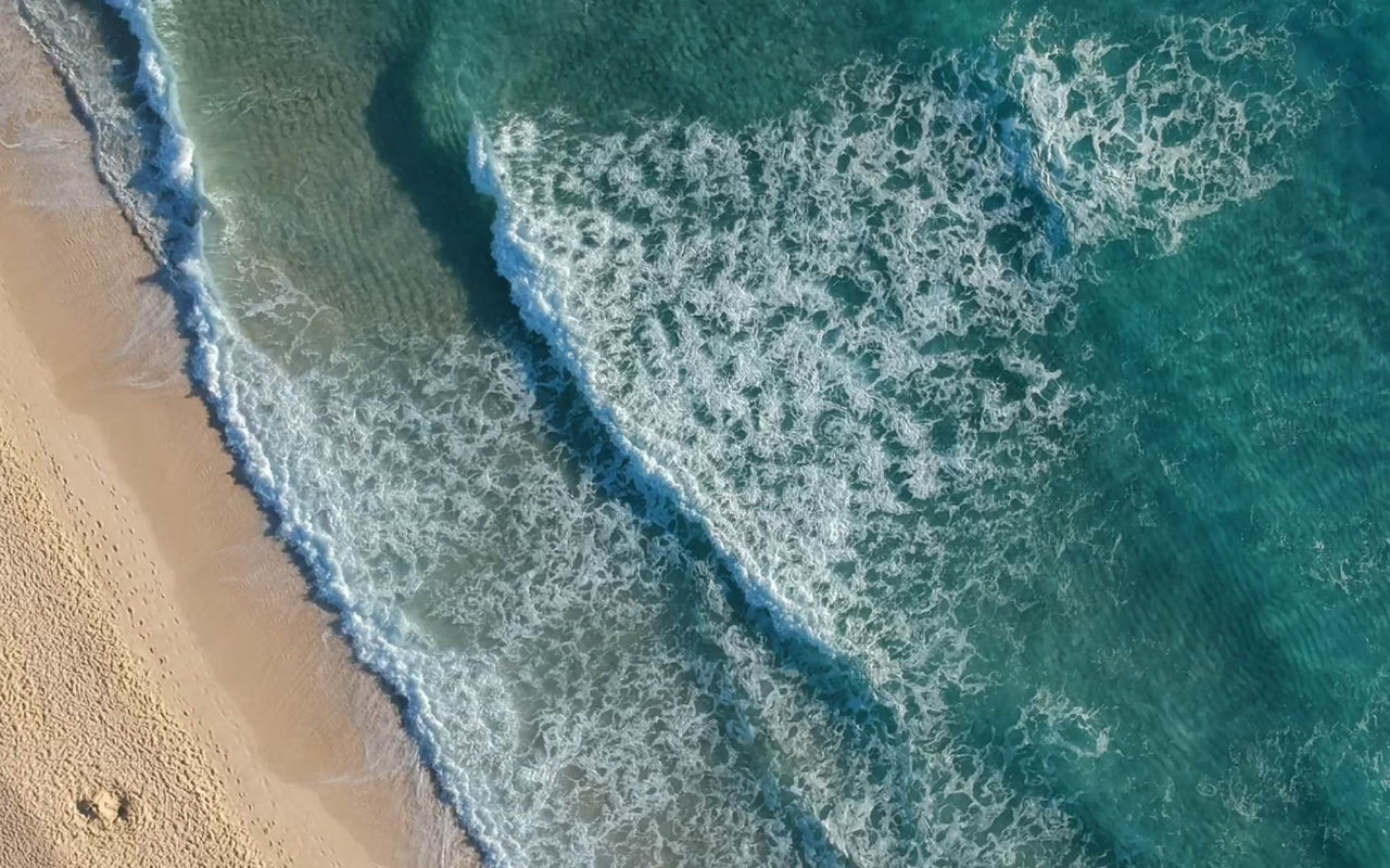 Vista aérea de uma praia com ondas a quebrar na areia dourada, num hotel do Pestana Hotel Group