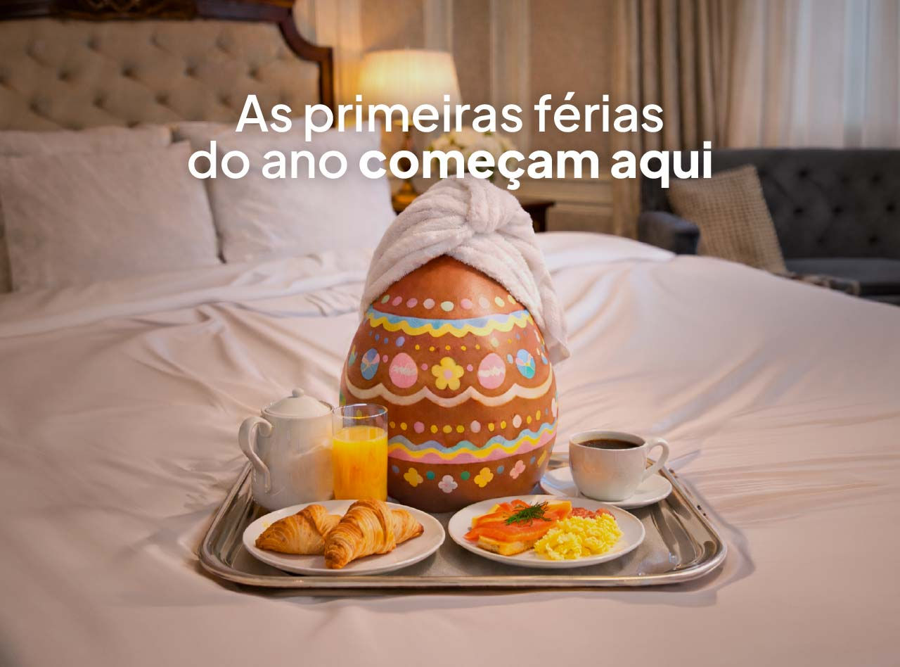 Bandeja de café da manhã sobre a cama com ovo de Páscoa decorado, croissants, café e suco em quarto iluminado