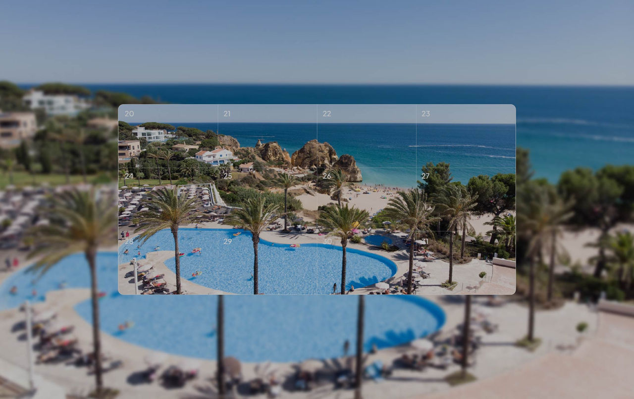 Vista elevada de piscina cercada por palmeiras diante de praia com falésias rochosas e mar azul ao fundo