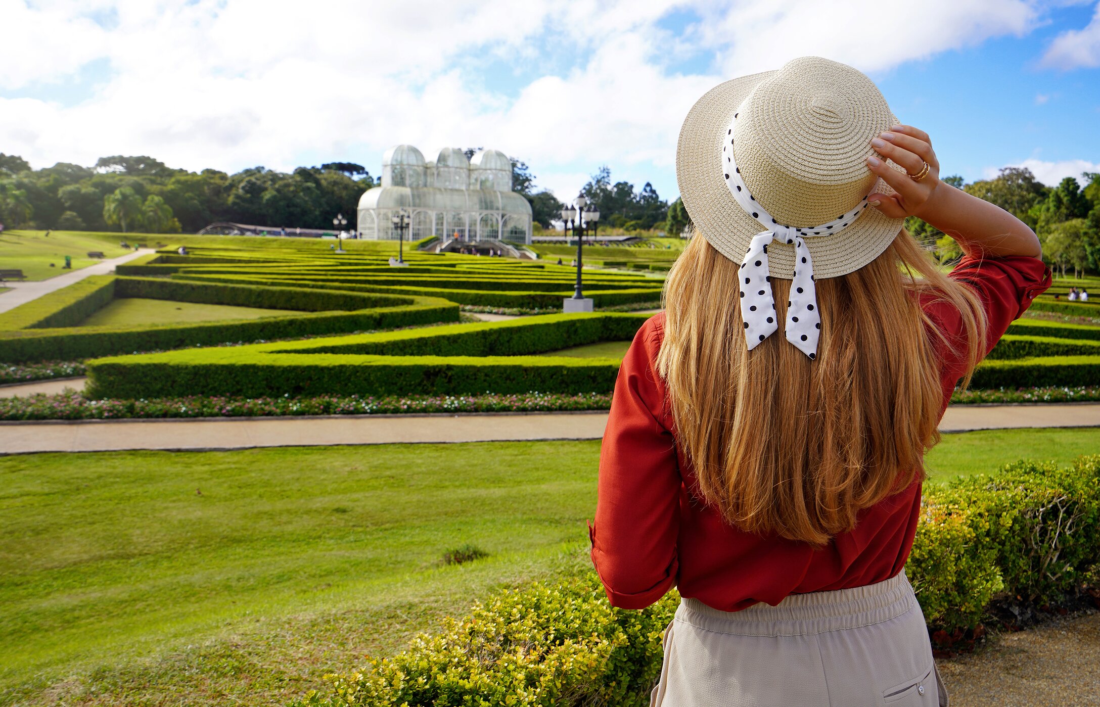 Frau mit Hut bewundert den Botanischen Garten von Curitiba, Brasilien, umgeben von Gras und Vegetation