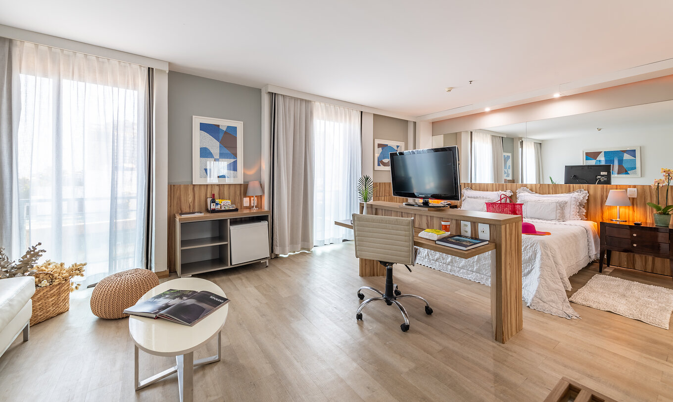 Die Junior Suite mit seitlichem Meerblick hat ein Doppelbett, einen Schreibtisch, Fernseher und zwei Fenster mit Vorhängen 