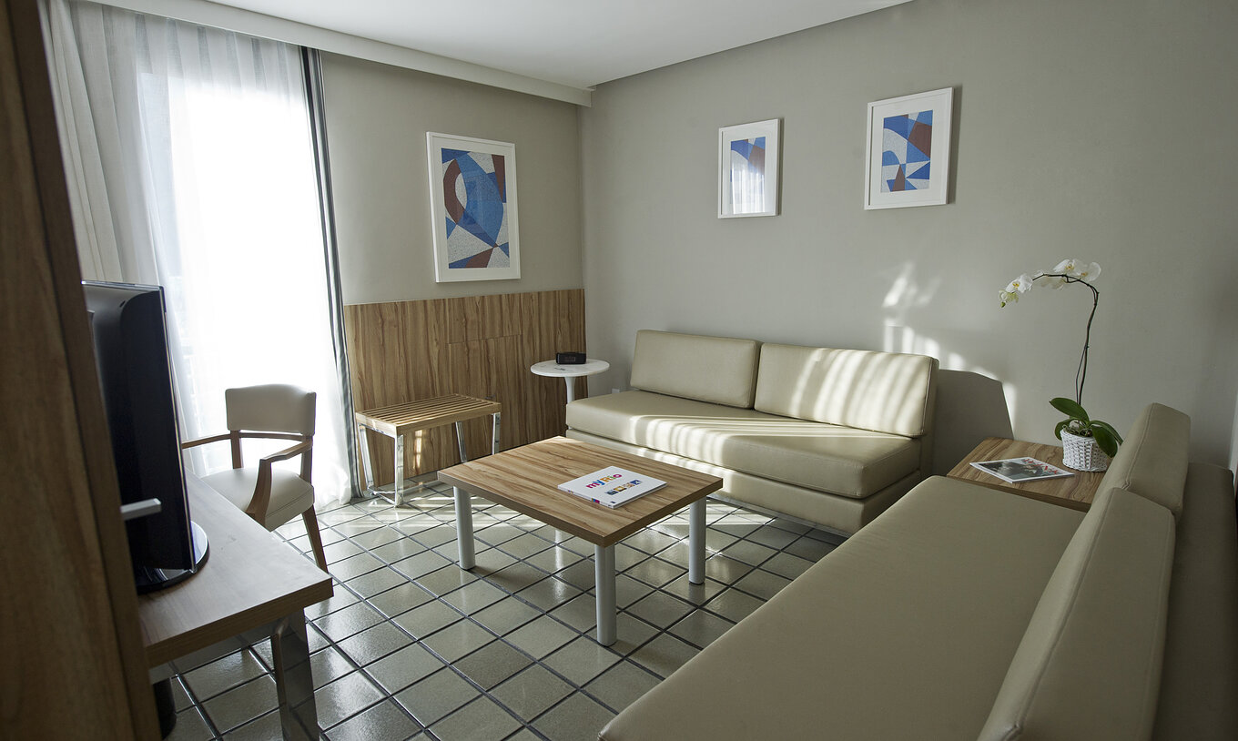 Die Standard-Suite hat ein Zimmer mit zwei beigen Sofas, einem Beistelltisch und einem Fernseher 