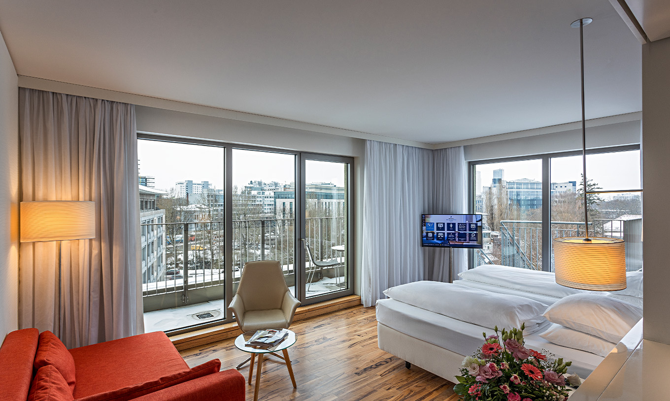 Das Premium Zimmer mit Panorambalkon im Pestana Berlin Tiergarten hat ein Sofa mit Lampe, Fernseher und ein Bett