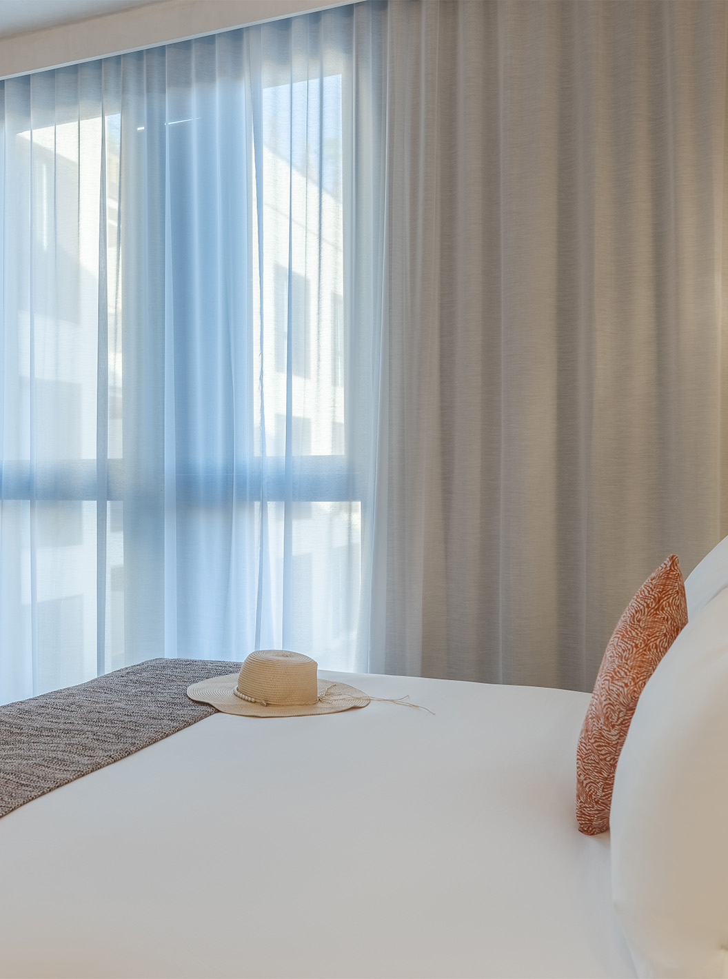 CR7 Suite im Pestana CR7 Marrakech mit hellem Bett, Strohhut und bodentiefen Vorhängen vor lichtdurchlässigen Gardinen