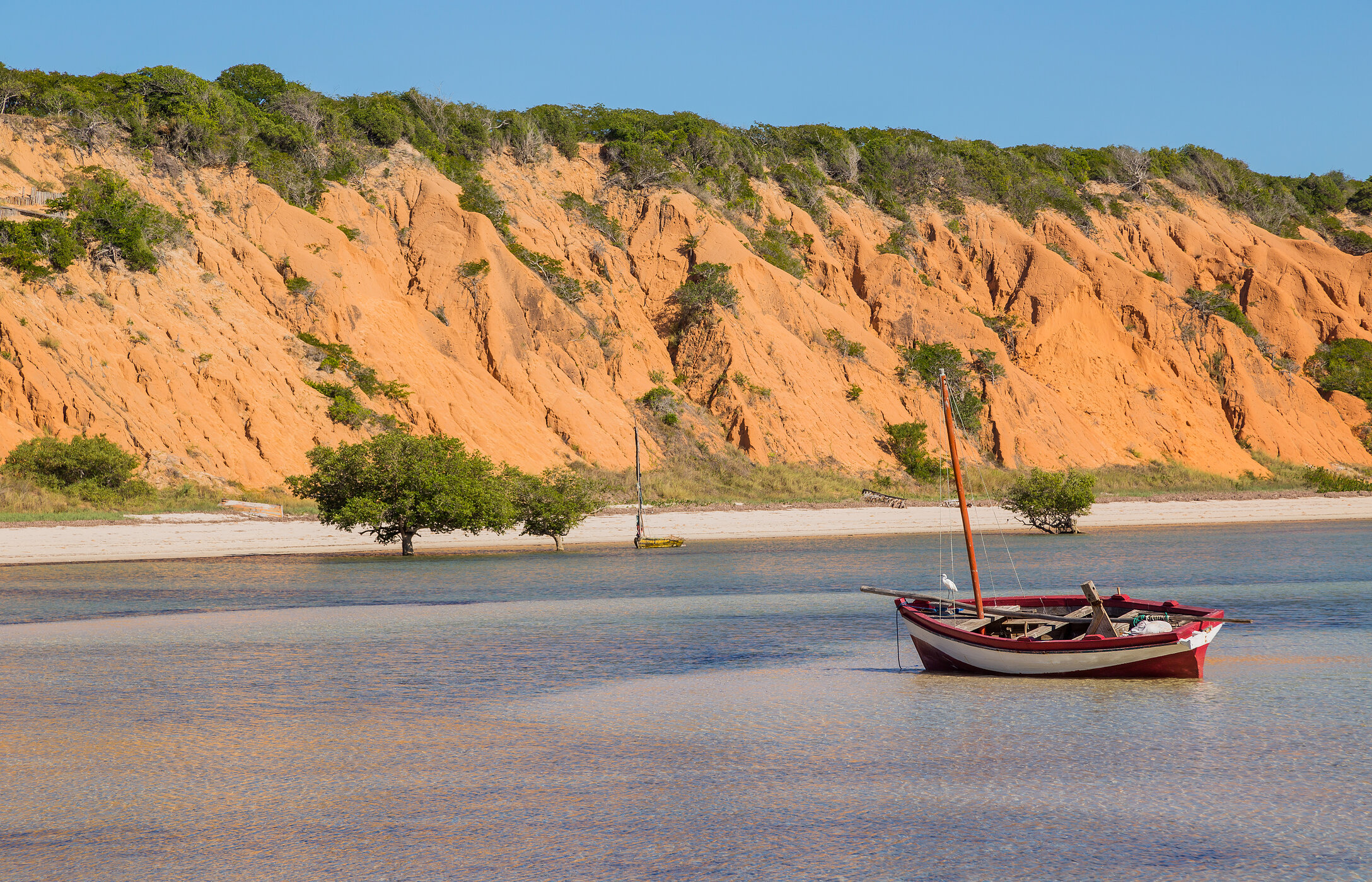 Meerblick von der Insel Magaruque mit einem traditionellen Boot vor Anker und rötlichen Klippen im Hintergrund