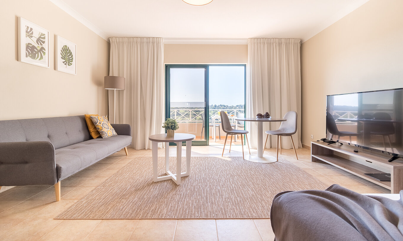 Das Studio im Pestana Gramacho Residences hat ein Wohnzimmer mit grauem Sofa, TV, Tisch und hellem Balkon