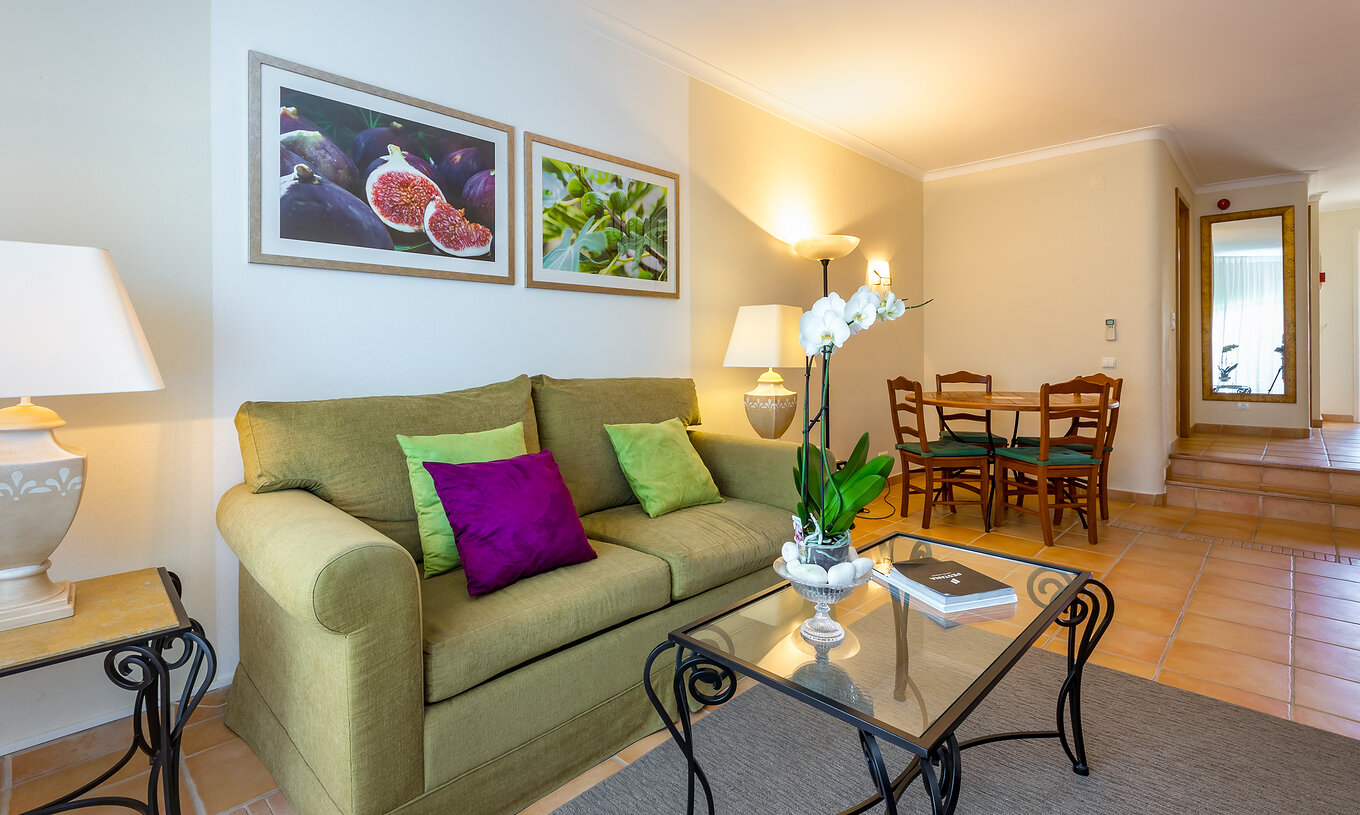 Das T2 Standard Appartement im Pestana Palm Gardens hat ein Wohnzimmer mit Sofa, Kissen, einem runden Tisch und Bildern
