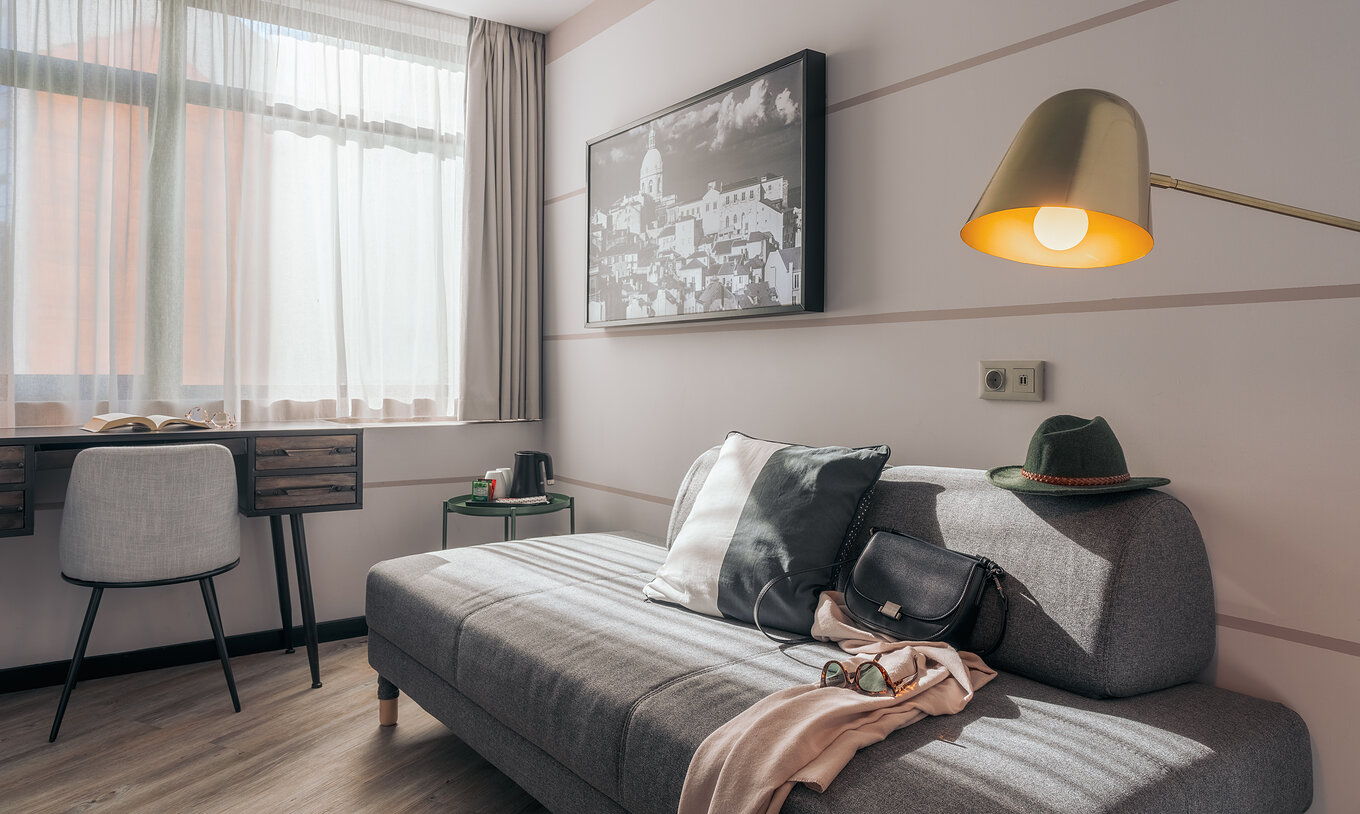 Das Double Superior im Pestana Lisboa Vintage hat graues Sofa, Schreibtisch mit Stuhl, Tisch und Bild