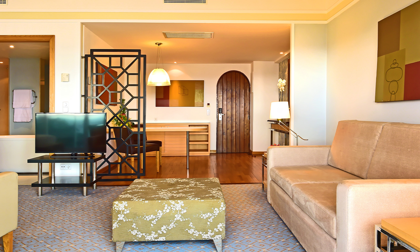 Die Junior Suite im Pestana Carlton Madeira hat ein Wohnzimmer mit Sofa und Fernseher und einen Eingangsbereich