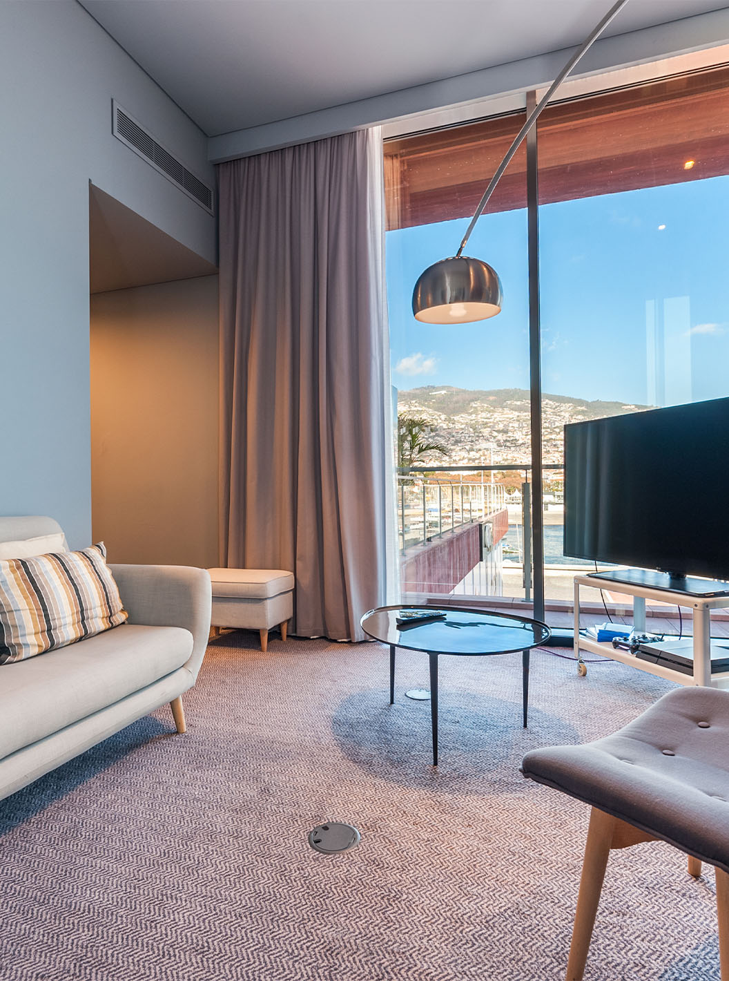 Die CR7 Suite im Pestana CR7 Funchal hat ein Wohnzimmer mit Sofa, Fernseher und Fenster mit Blick auf Funchal