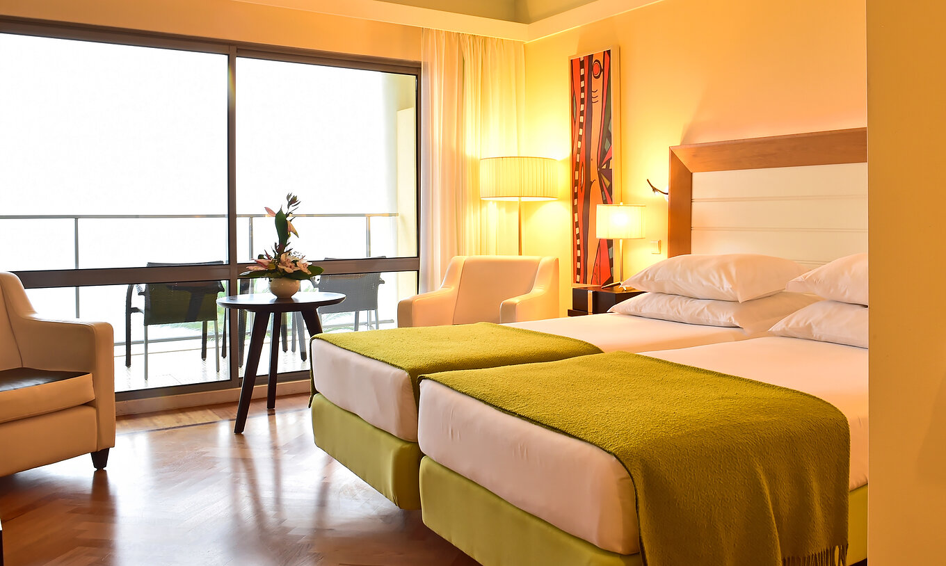 Das Superior Zimmer hat zwei Betten mit grünem Bettbezug und ein großes Fenster zum Balkon 