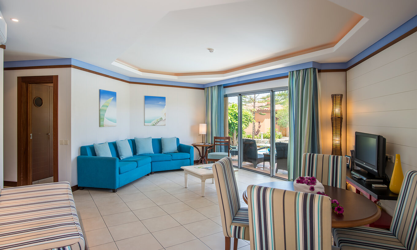 Die Pool Villa hat ein Wohnzimmer mit Fenster, Tisch und Stühlen, Sofa und Fernseher 