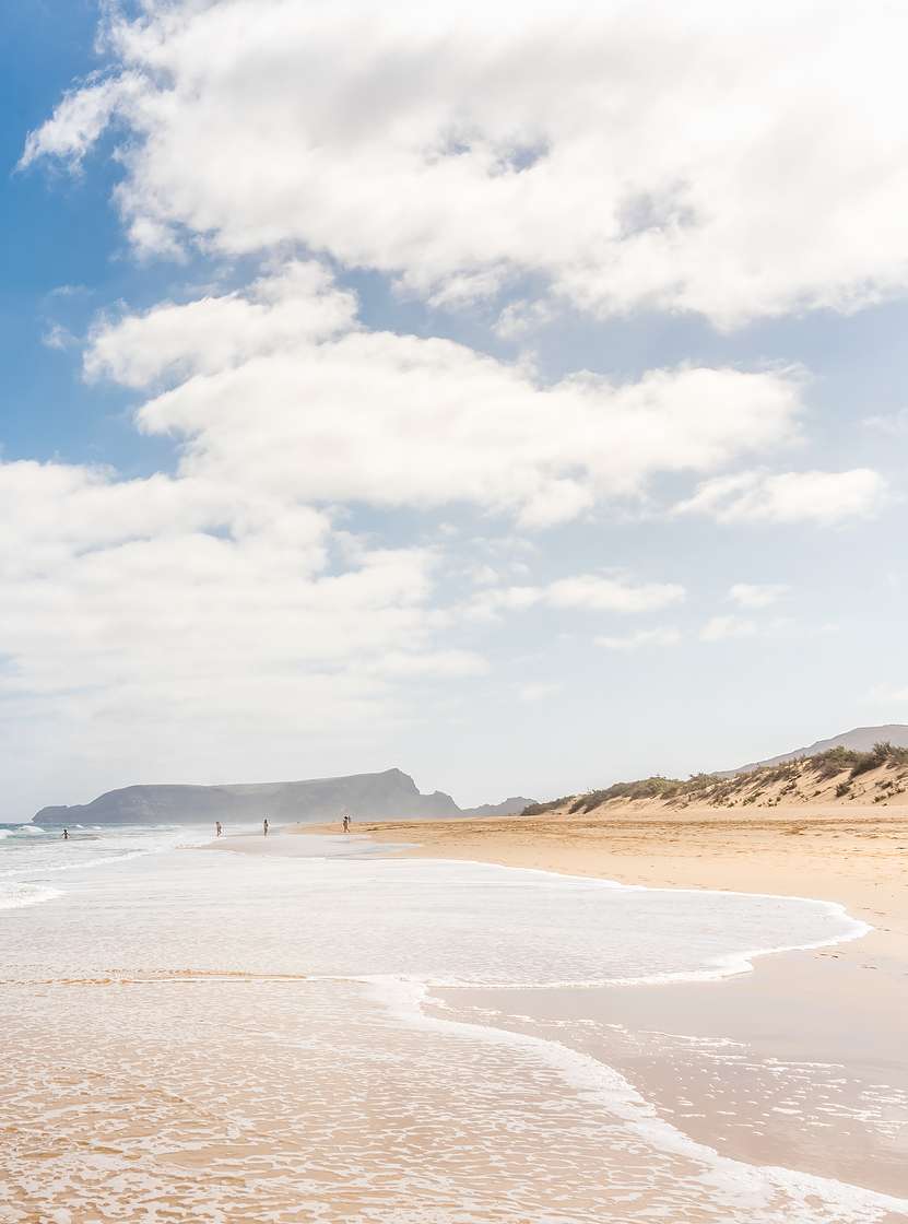 Langer Strand in Porto Santo mit hellem Sand, ruhigen Wellen und blauem Himmel mit einigen Wolken