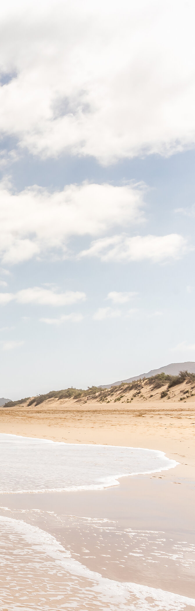 Langer Strand in Porto Santo mit hellem Sand, ruhigen Wellen und blauem Himmel mit einigen Wolken