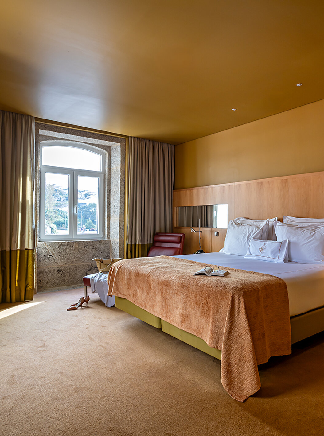Die Junior Suite verfügt über ein Doppelbett mit einer beigen Decke und einem Steinfenster mit Flussblick