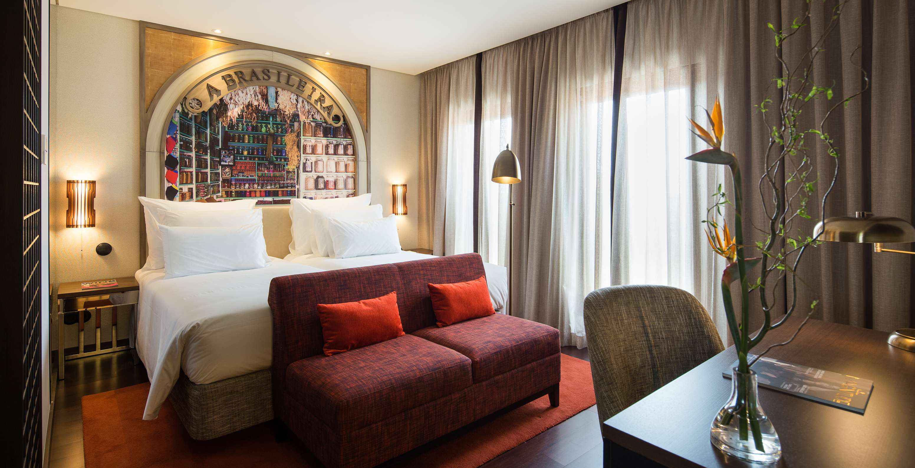 Signature Zimmer im Pestana A Brasileira Porto mit großem Bett, roten Sitzmöbeln und hohen Fenstern bei Tageslicht