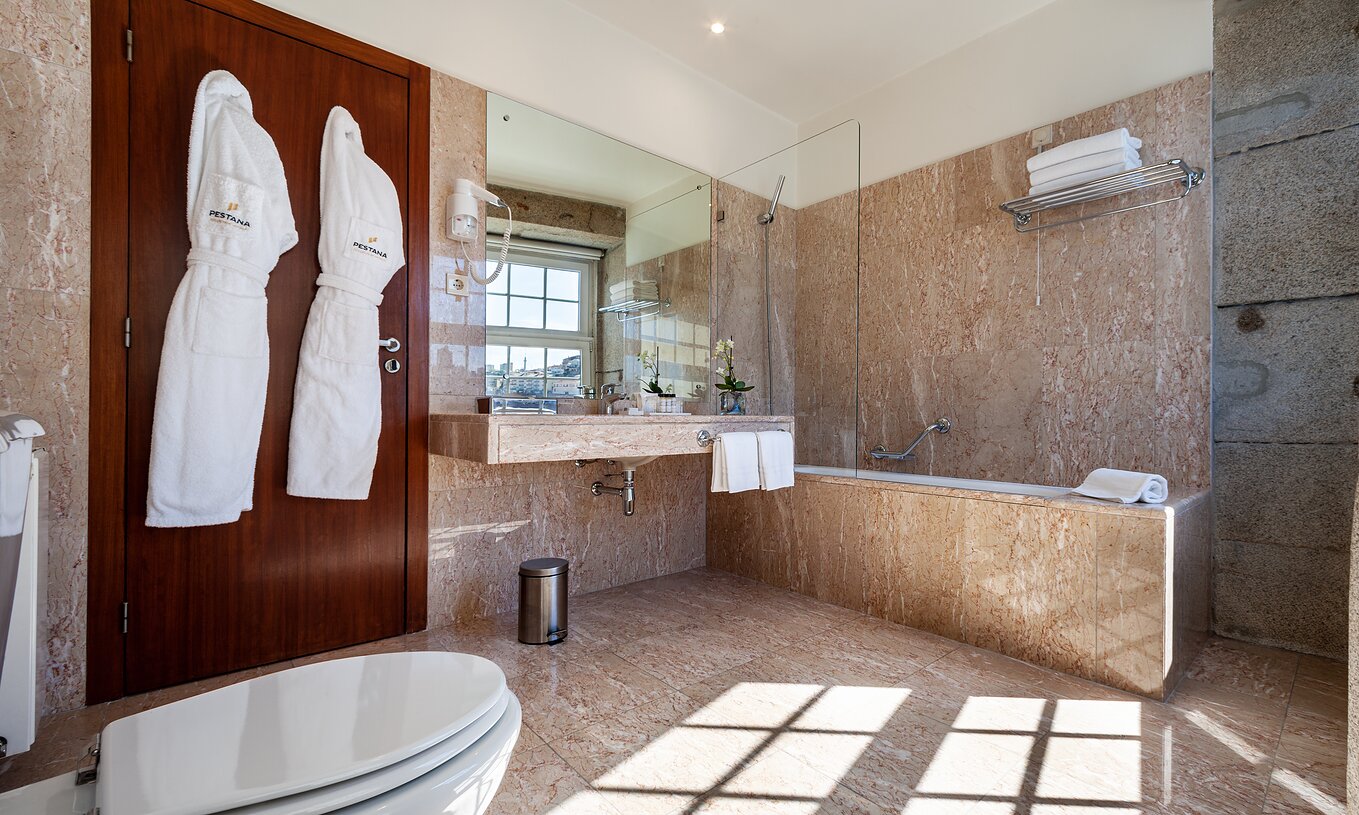 Plaza Pestana Vintage Porto hat ein Badezimmer mit Badewanne, zwei Bademänteln, Waschbecken und Haartrockner