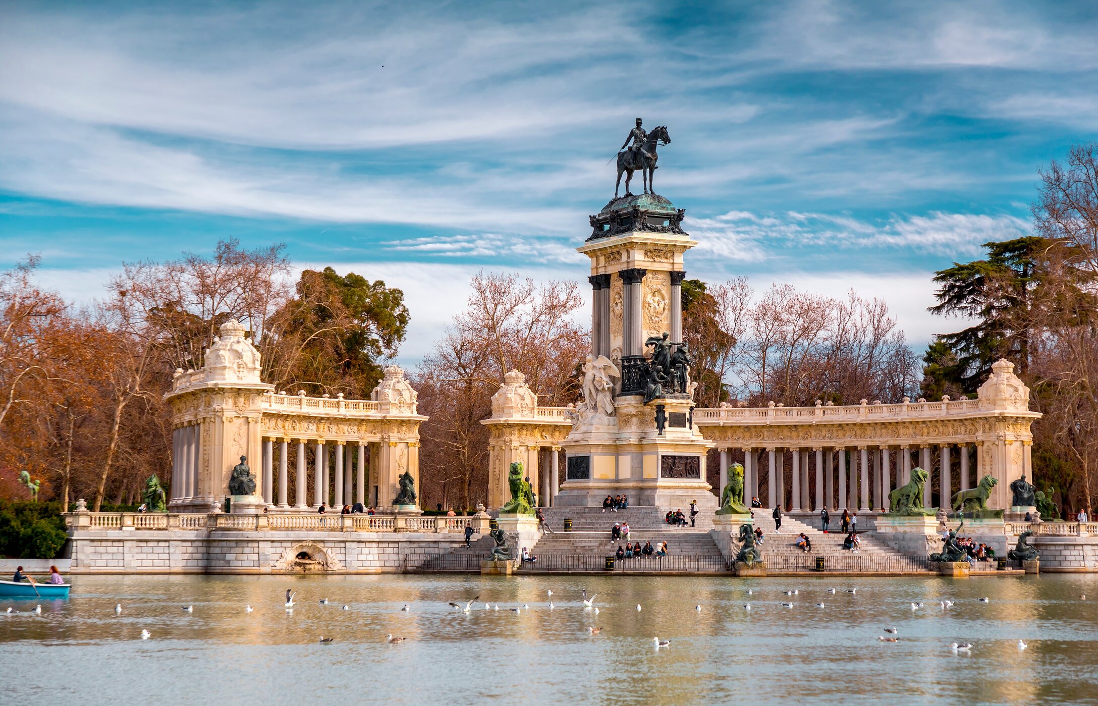 See im Retiro-Park im Zentrum von Madrid, mit mehreren Menschen, die auf den Stufen ruhen und Vögeln, die auf dem See sitzen