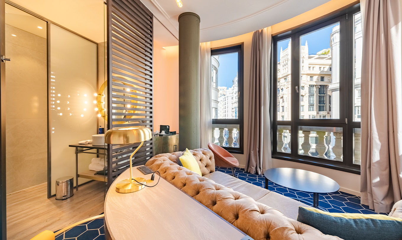 Das Fantastic 7 Zimmer im Pestana CR7 Gran Vía Madrid hat ein Sofa mit einem Tisch und große Fenster zu den Gebäuden