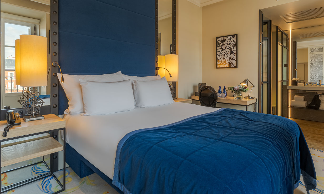 Deluxe Plaza Mayor Zimmer im Pestana Collection Plaza Mayor mit blauem Bett, Schreibtisch und offenem Bad
