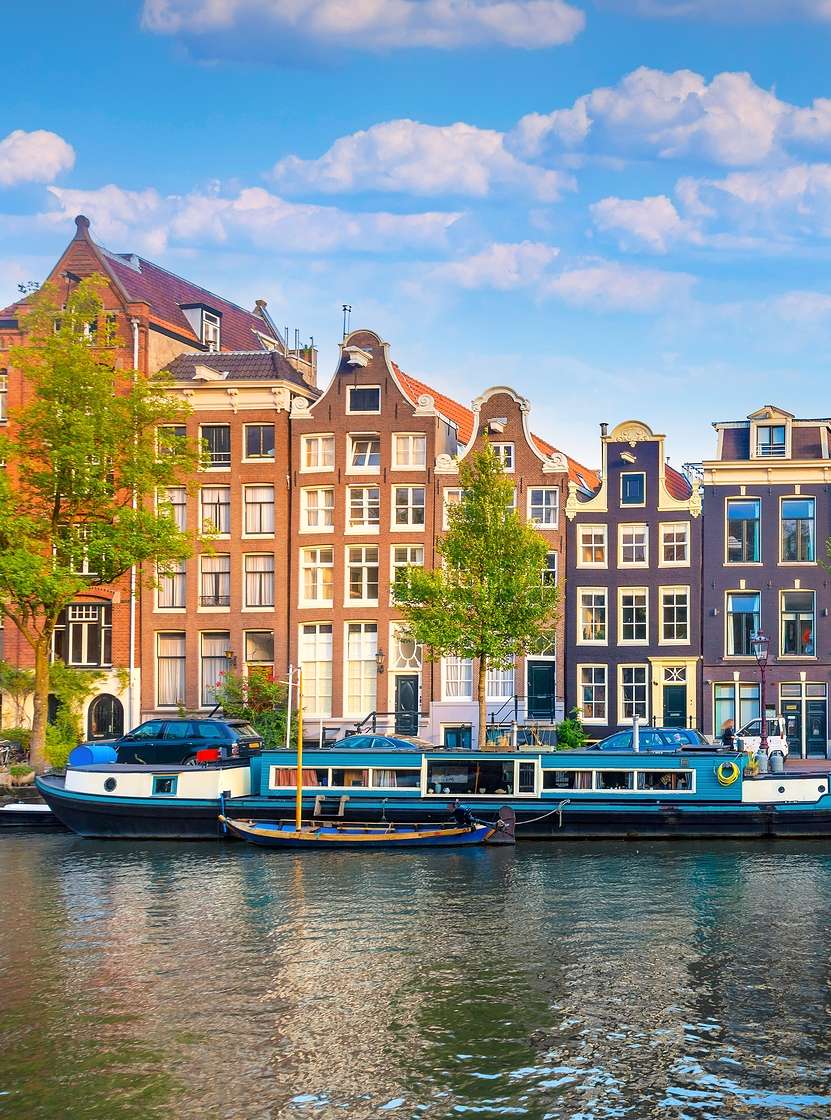 Amsterdamer Kanal mit Menschen, die am Ufer spazieren gehen, Boote und typische Gebäude unter blauem Himmel