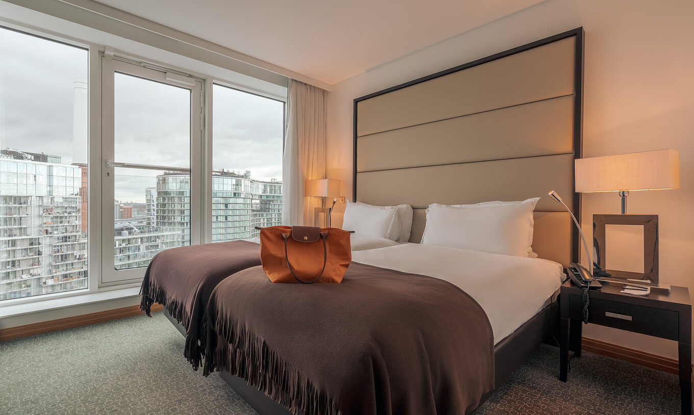 Das Superior Twin im Pestana Chelsea Bridge hat Doppelbett, Nachttische, Lampe und Fenster mit Stadtblick