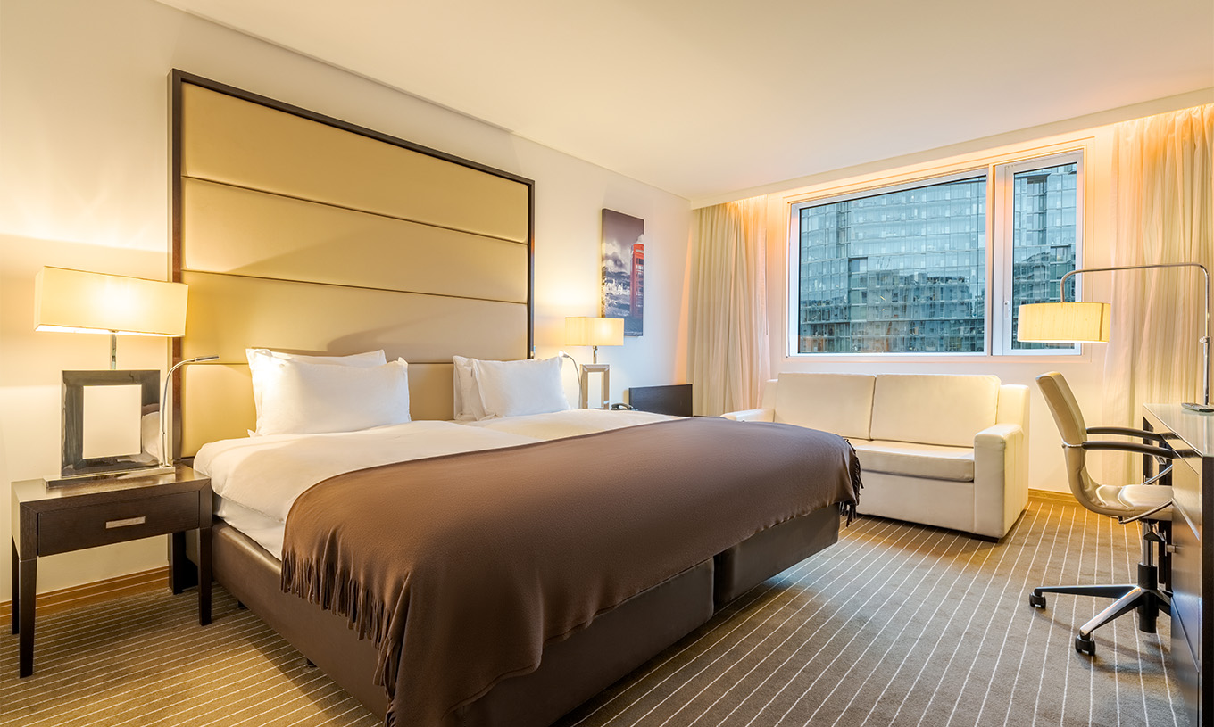 Das Twin Deluxe im Pestana Chelsea Bridge hat zwei Betten, Nachttisch, Sofa, Lampen und Fenster mit Vorhängen