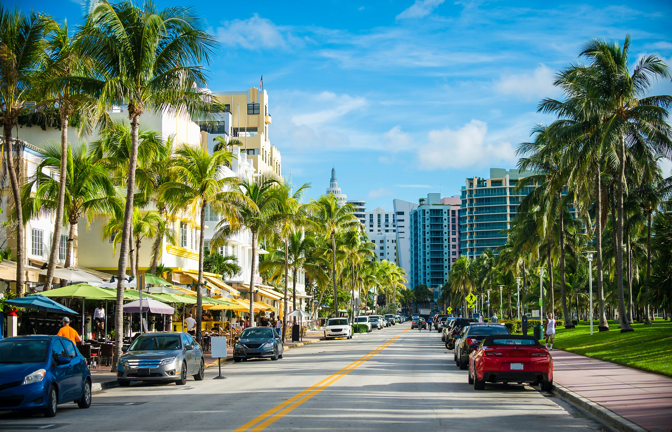 Blick über die Ocean Drive in Miami, mit hohen Palmen, Art-Deco-Gebäuden und mehreren geparkten Autos