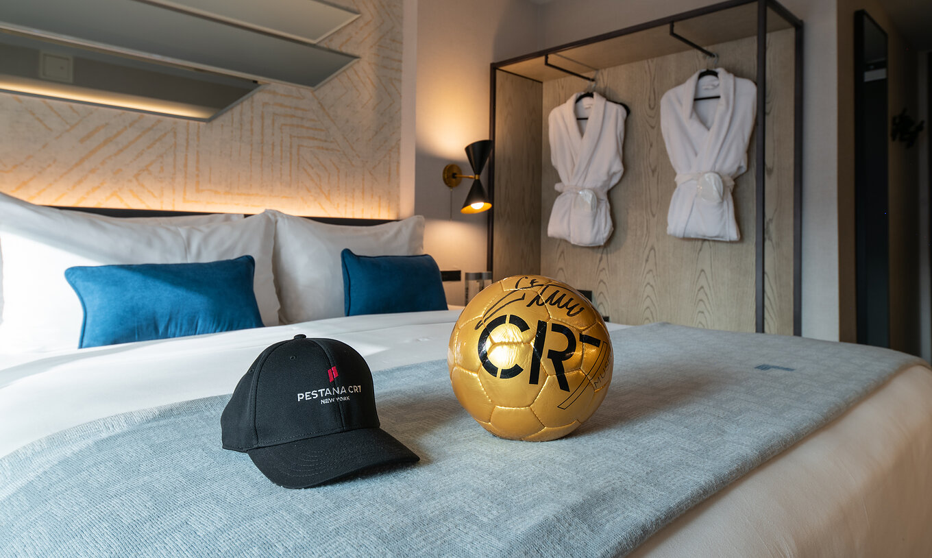 Das Deluxe King Room im Pestana CR7 Times Square hat ein Doppelbett mit einem CR7-Ball und einem Hut