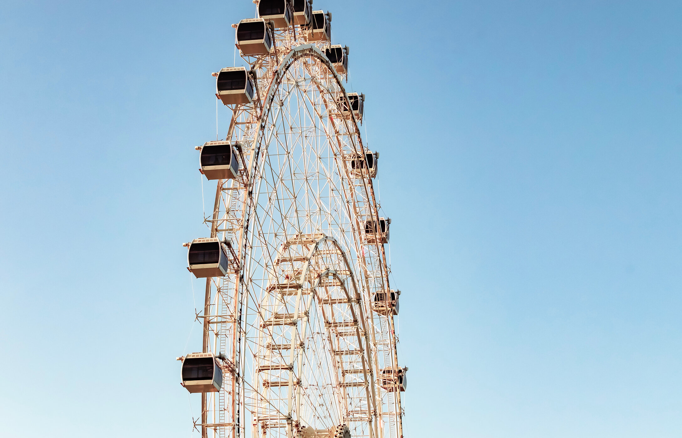 Blick auf ein Riesenrad mit weißen Kabinen und einem klaren blauen Himmel im Hintergrund