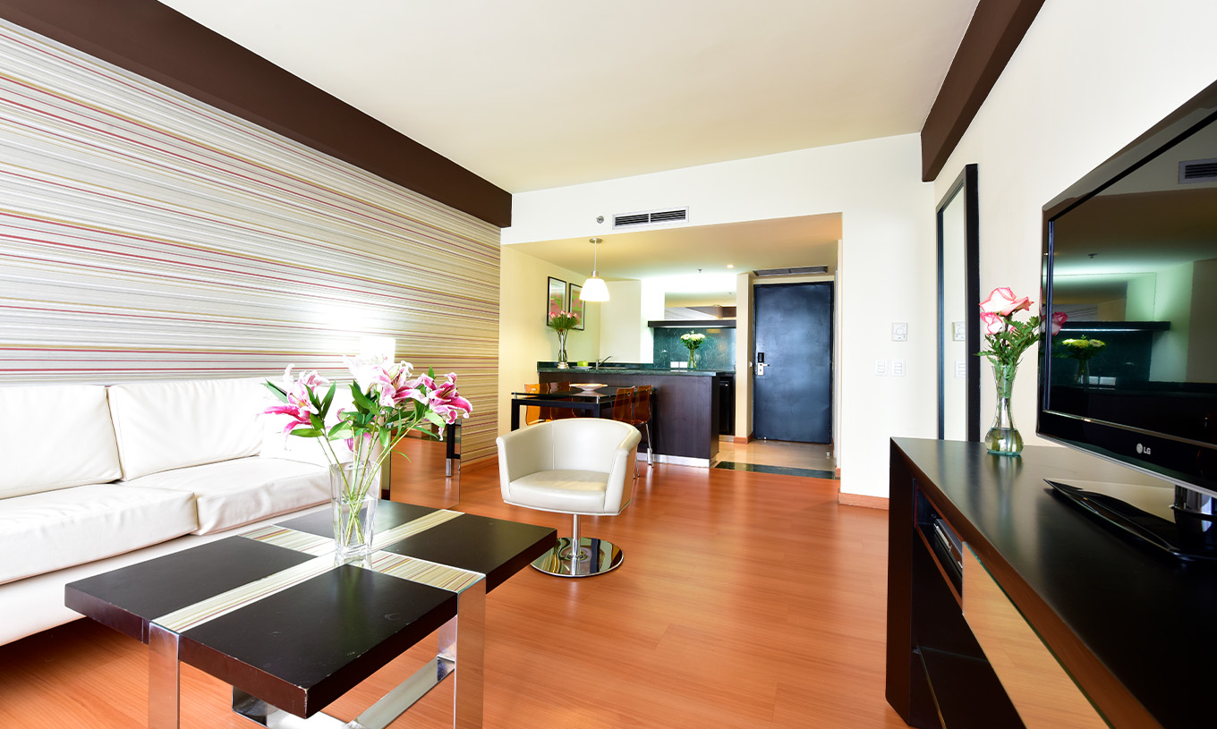 Die King Junior Suite im Pestana Caracas hat ein Wohnzimmer mit einem bequemen weißen Sofa, einem Tisch und einem Fernseher