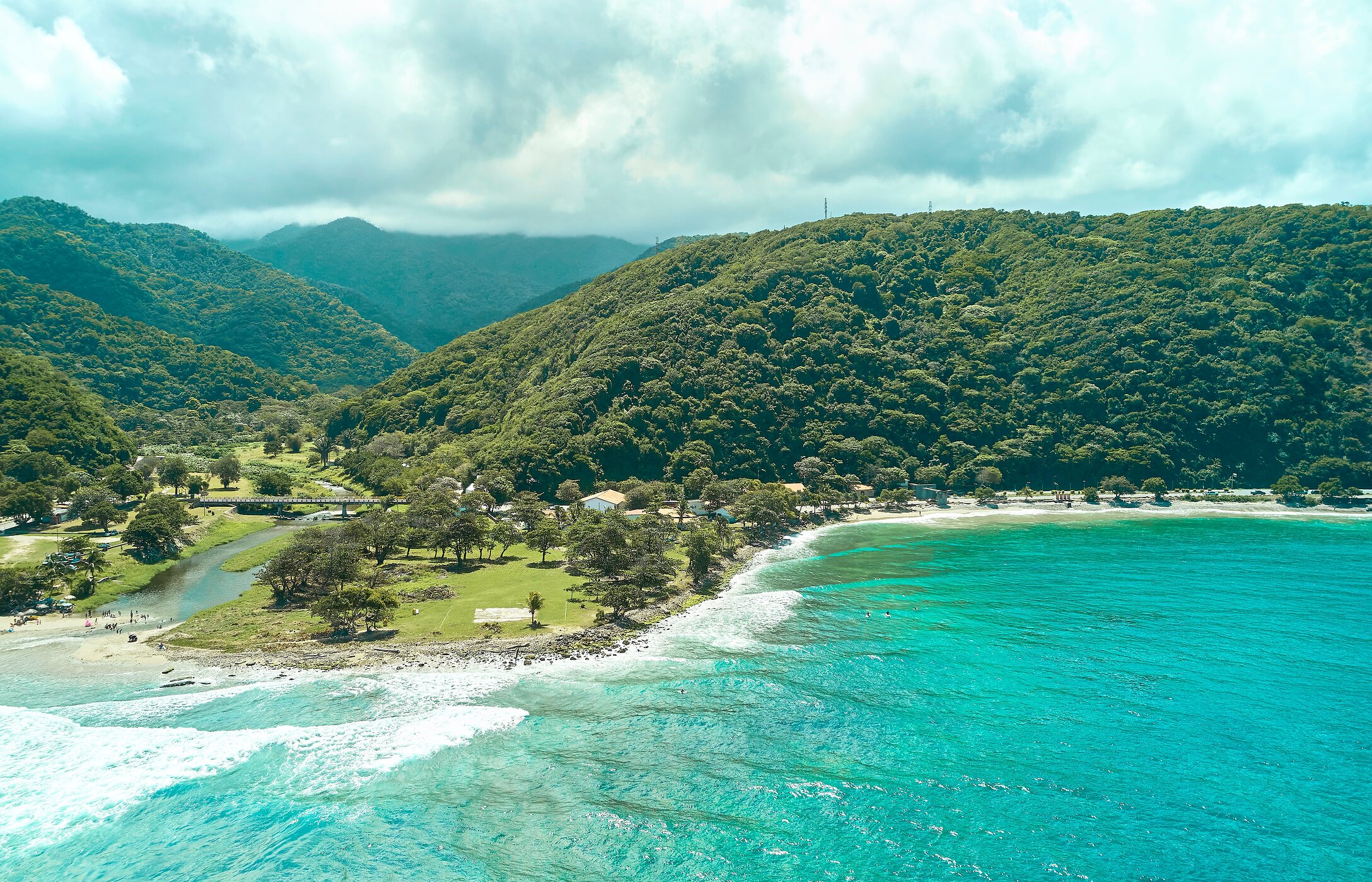 Luftaufnahme des Strandes La Punta in Venezuela, mit kristallklarem Wasser, umgeben von grünen Bergen.