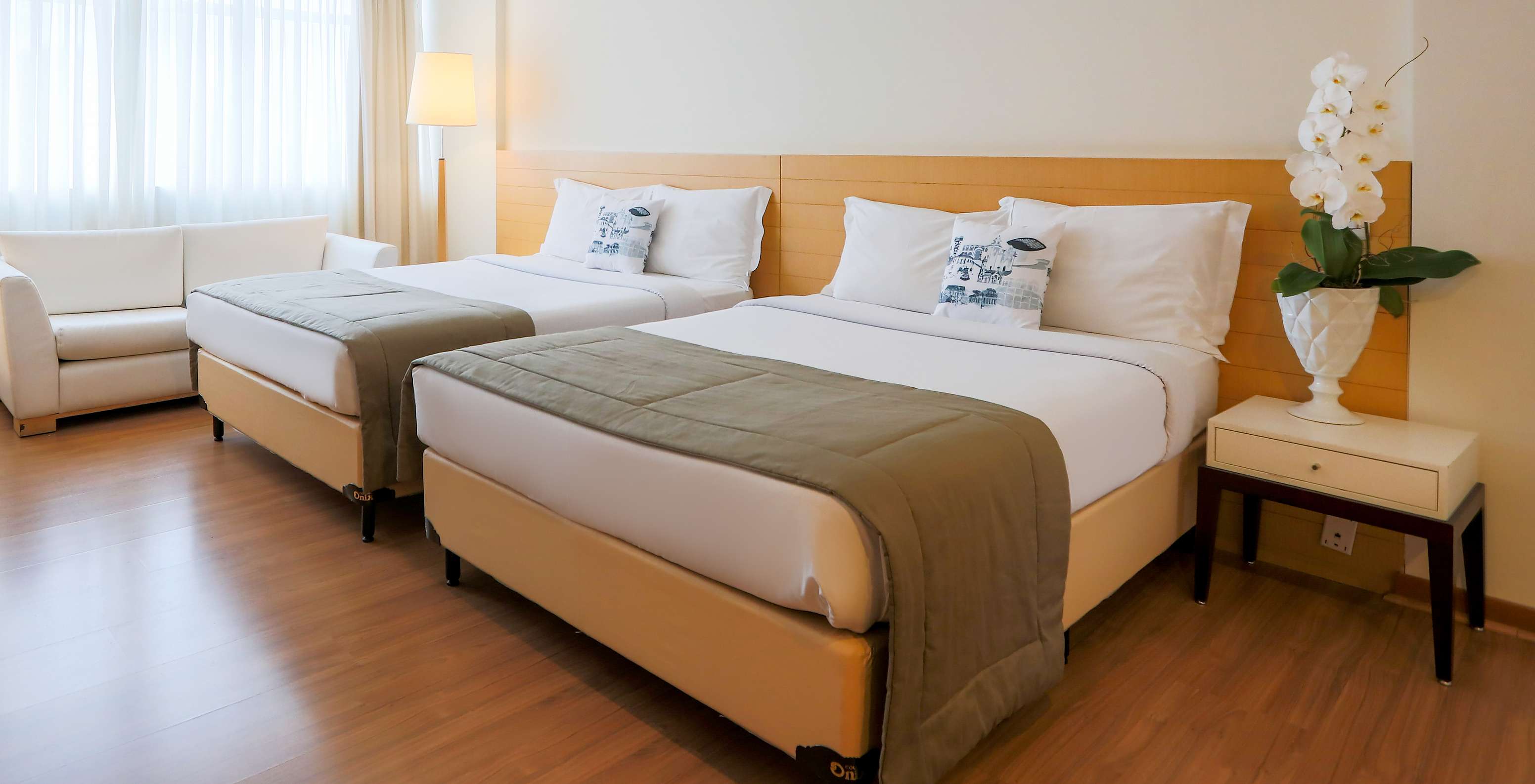 The Twin Standard at Pestana Curitiba has a clean decor in light wood tones, with a double sofa and a window