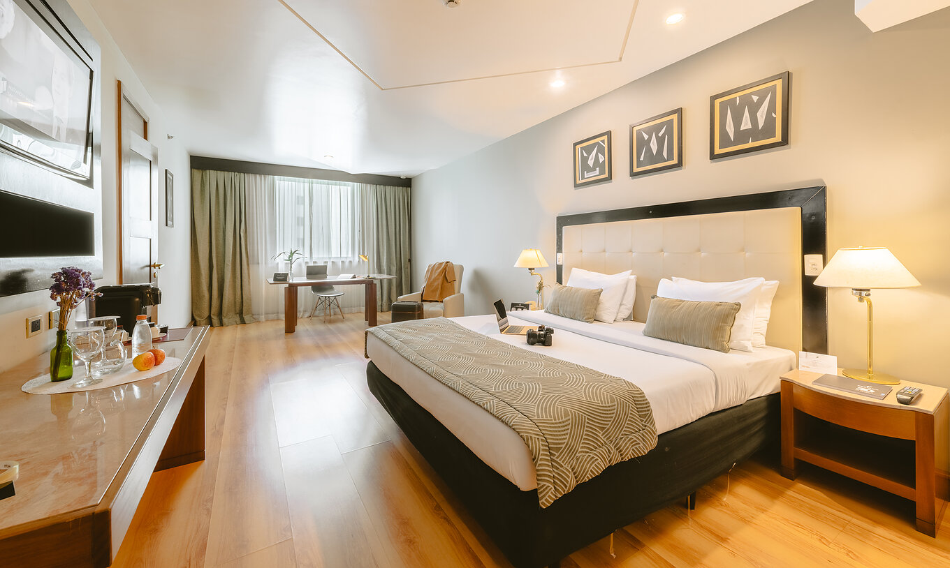 The Executive Suite of Pestana São Paulo has a room with a double bed, two bedside tables, a desk, and a window