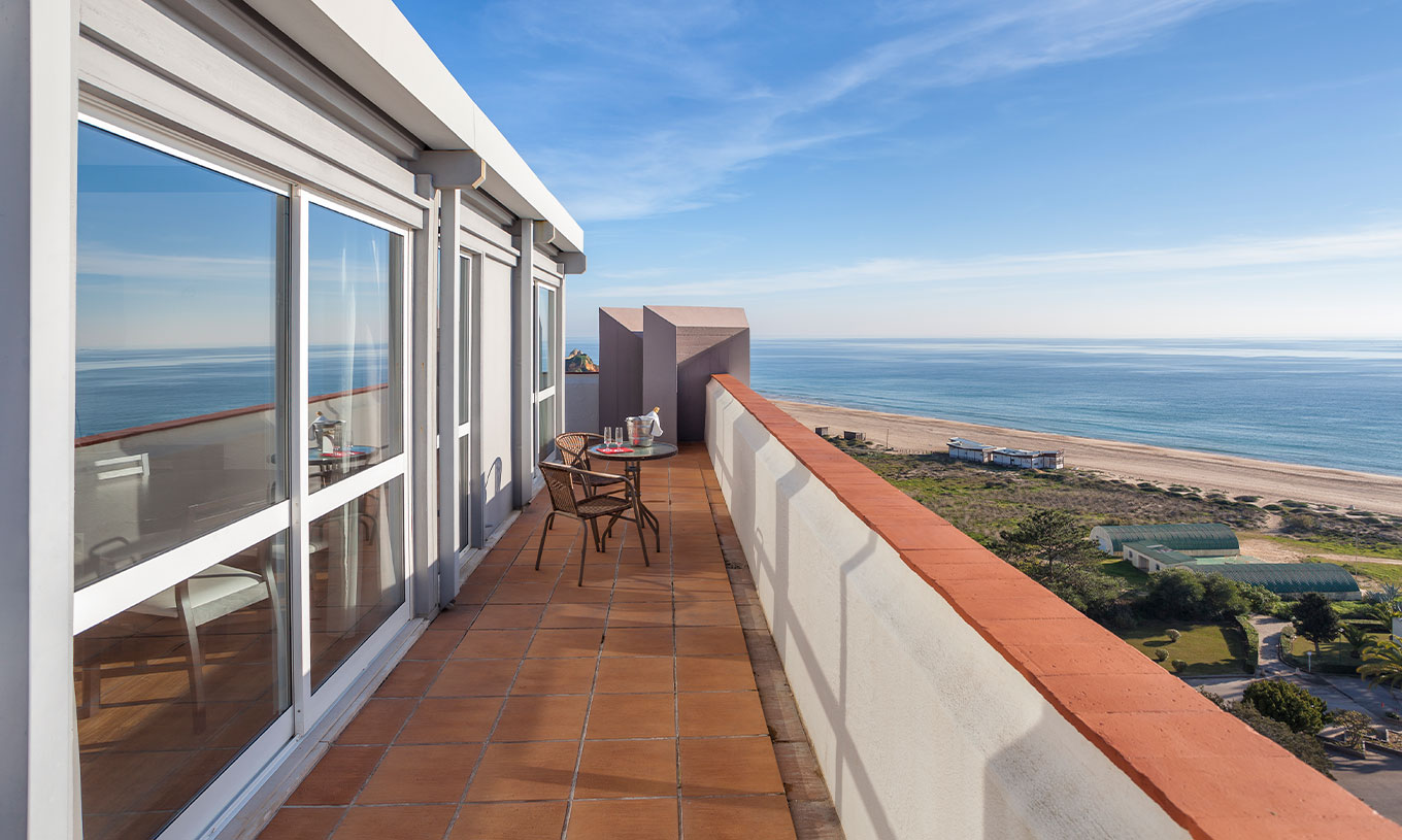 The T1 Sea View Apartment at Pestana Alvor Atlântico has a balcony with a table and two chairs, overlooking the beach and sea