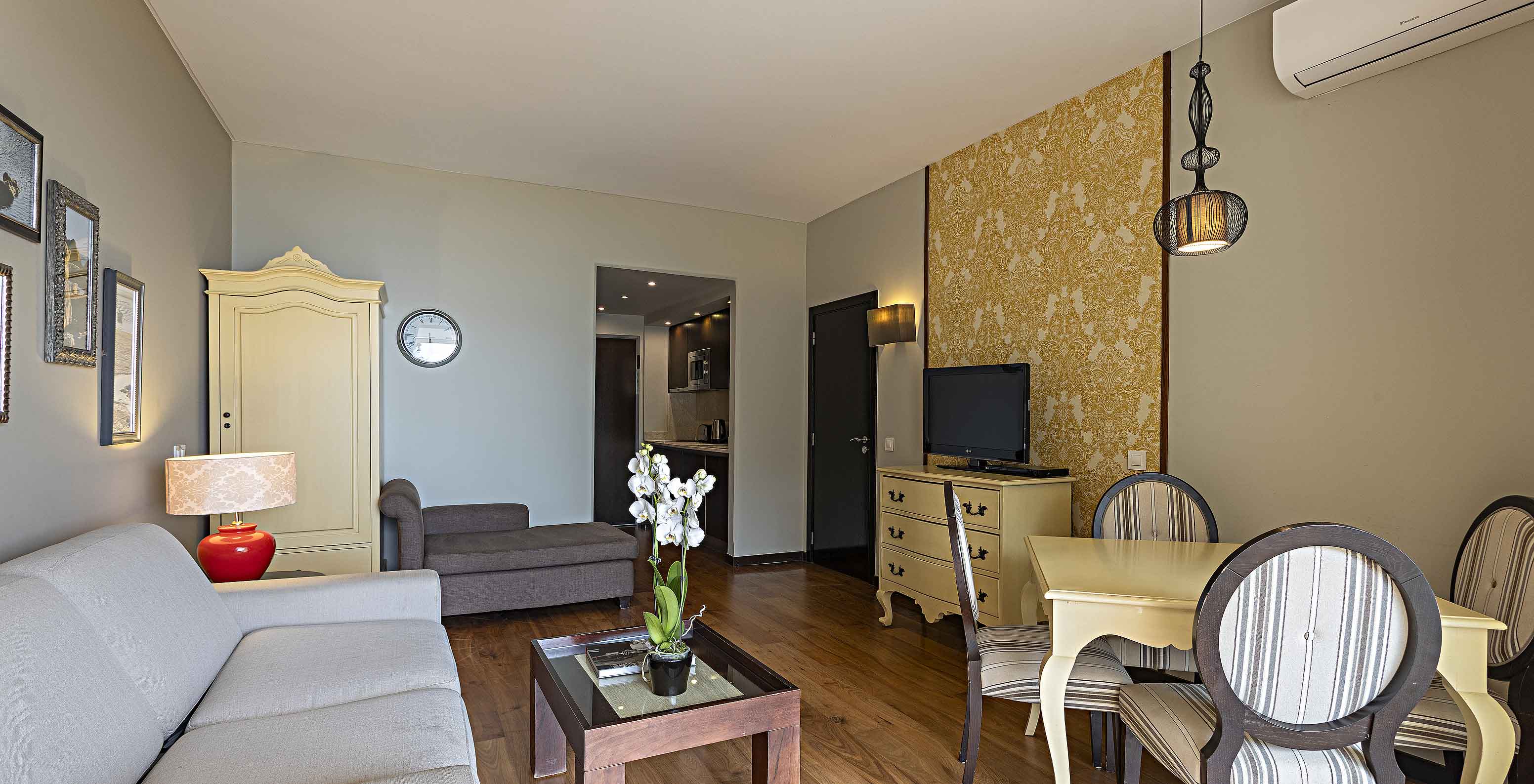 The Cliff Suite T1 at Pestana Alvor Praia has a living room with a sofa, wallpaper, television, and a dining table