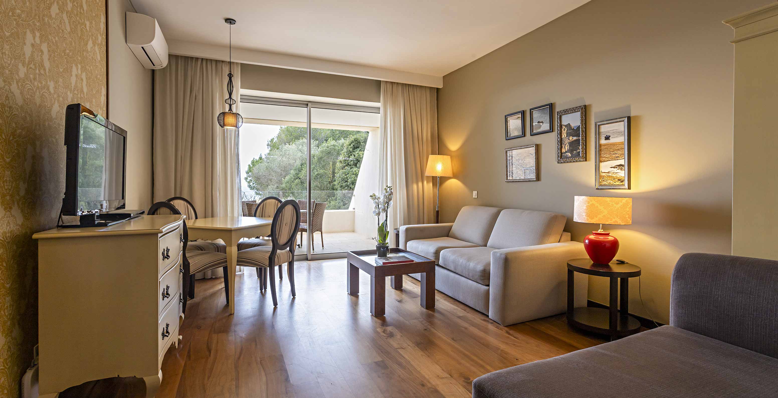 The Cliff Suite T1 at Pestana Alvor Praia has a living room with two sofas, a dresser with a TV, a dining table, and chairs