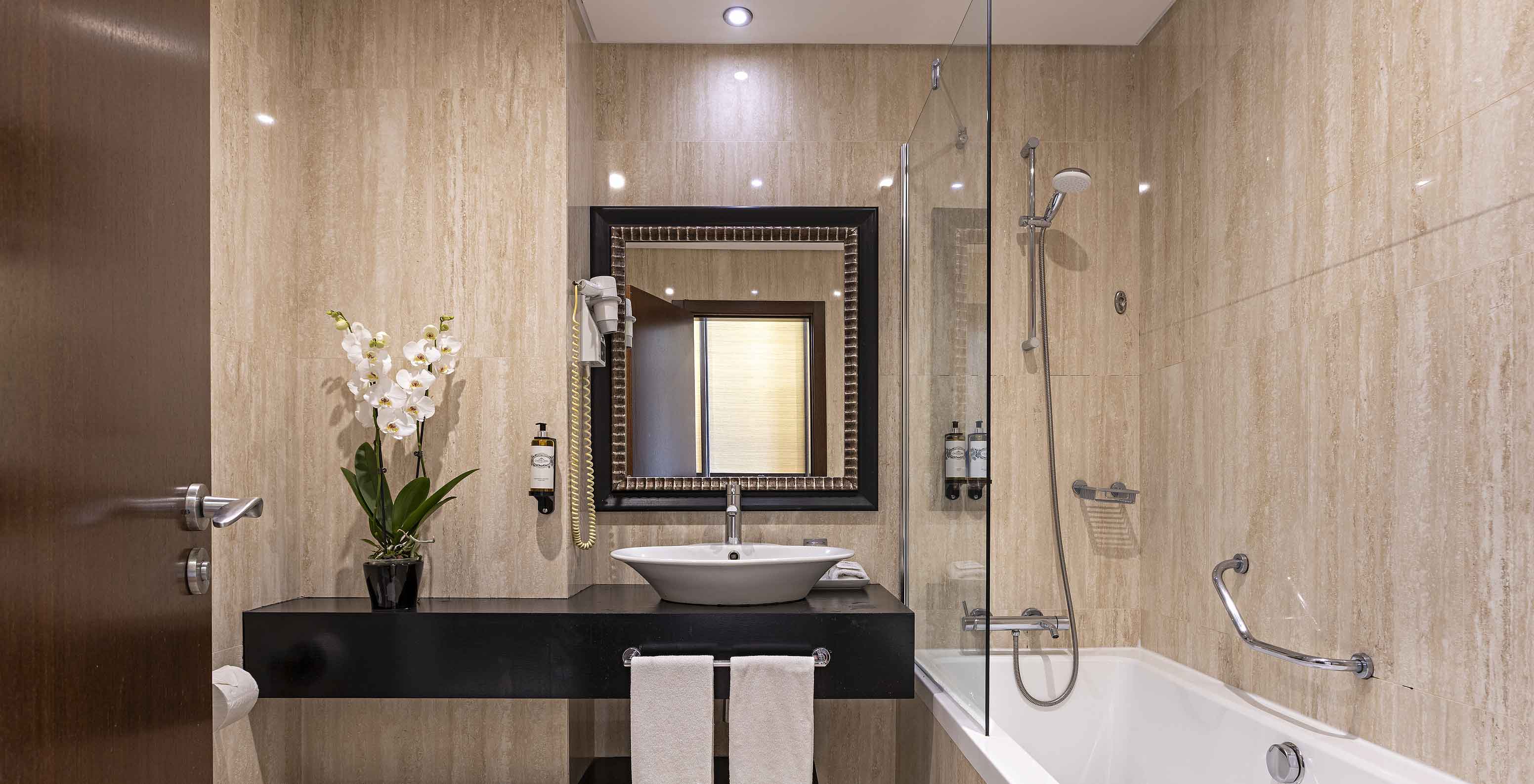 The Cliff Suite T2 at Pestana Alvor Praia has a modern bathroom with a bathtub, a sink, a toilet, a mirror, and flowers
