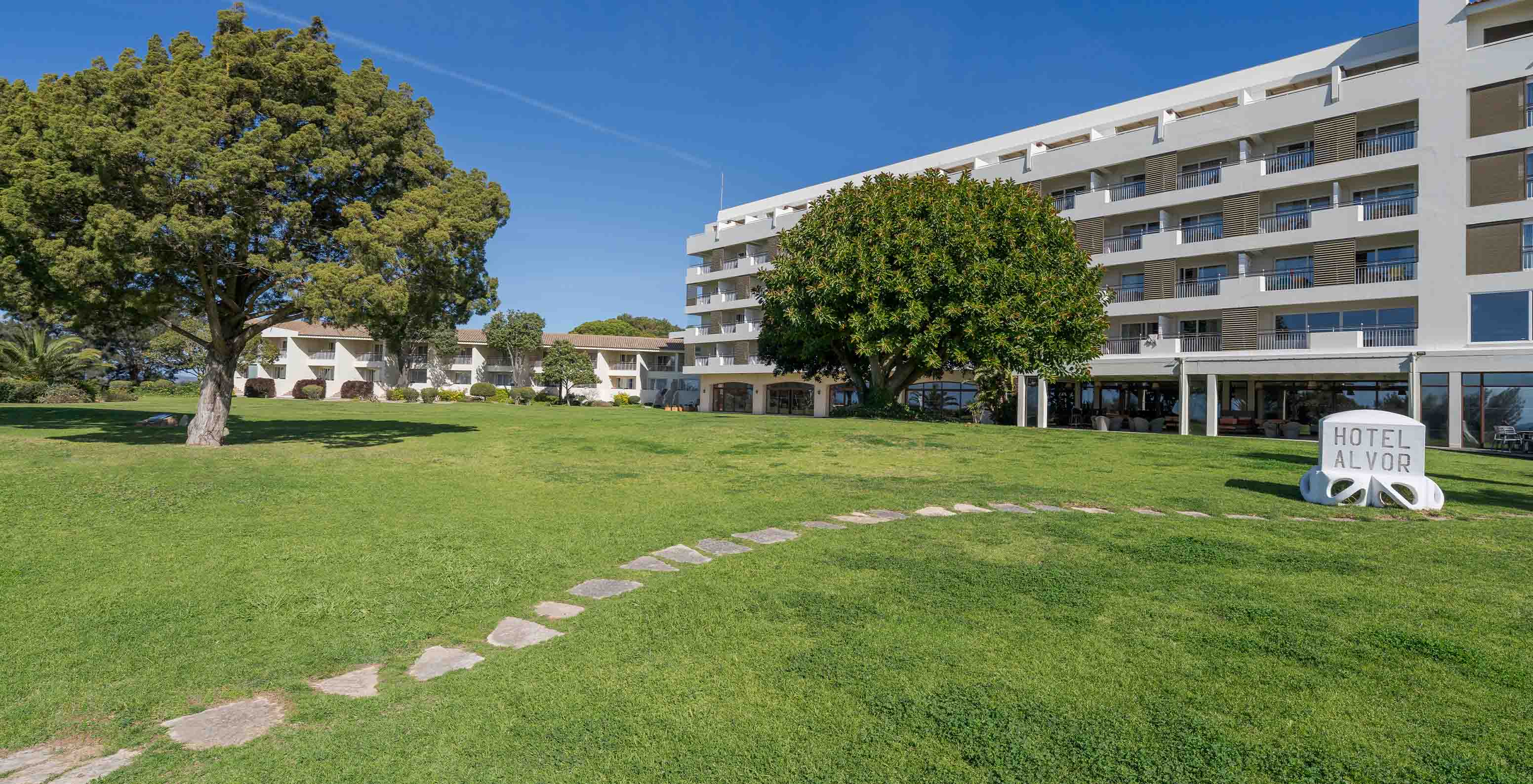 Pestana Alvor Praia garden with trees, hotel buildings behind, stone path